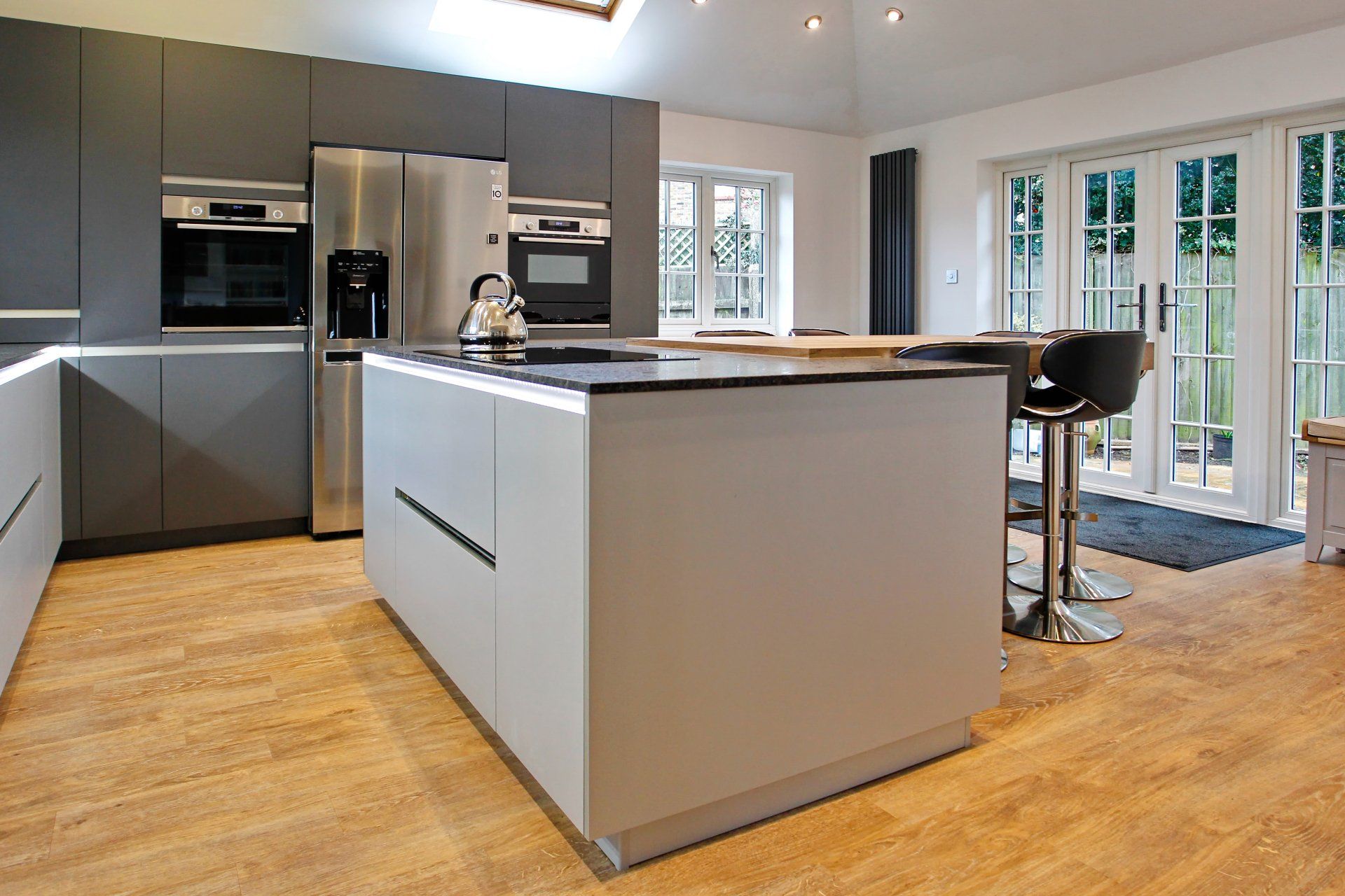 Modern kitchen with grey cabinetry, stainless steel appliances, and island with bar stools.