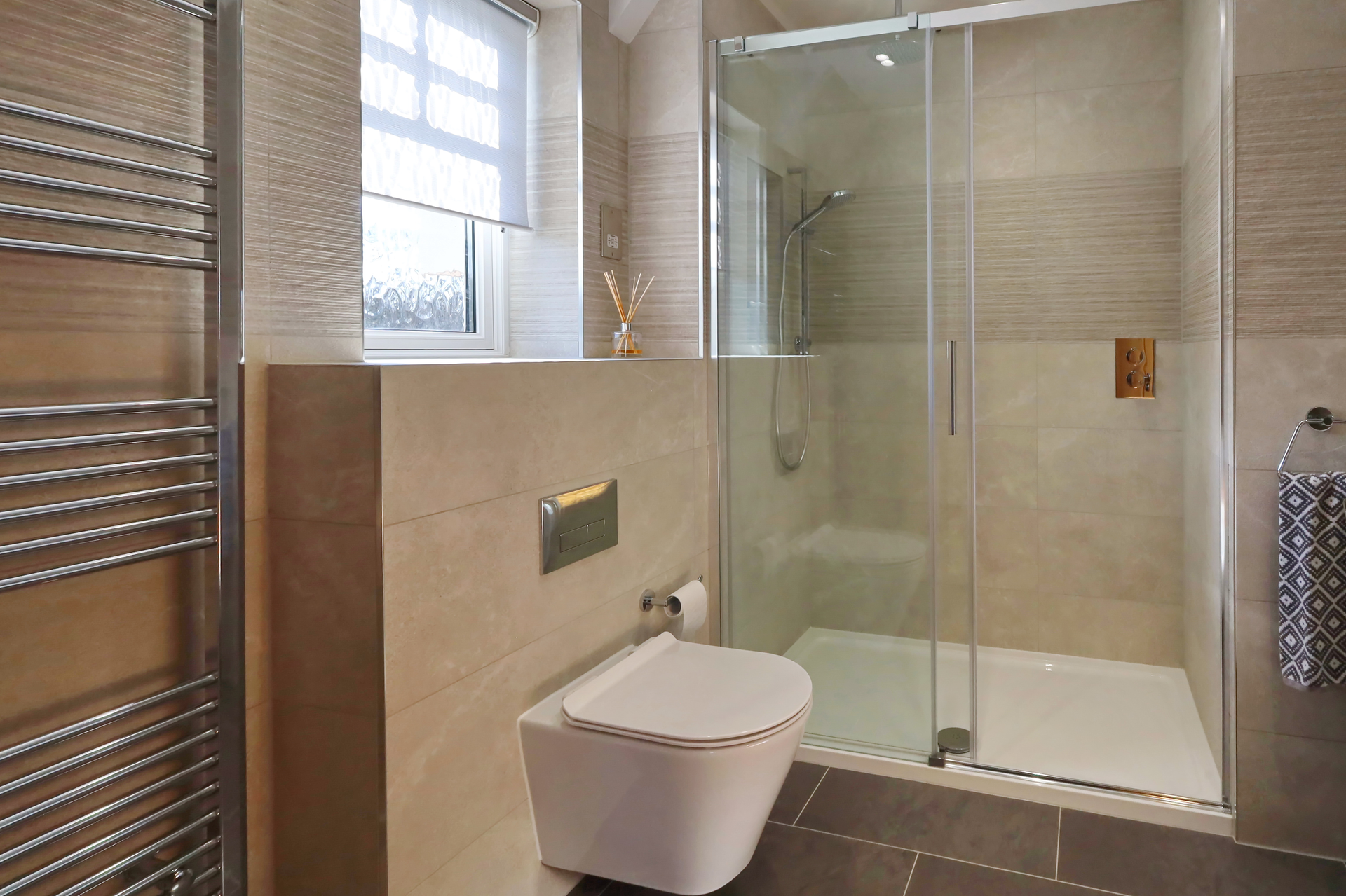 Modern bathroom with a glass shower, toilet, and towel warmer. Beige tile and dark gray floor.