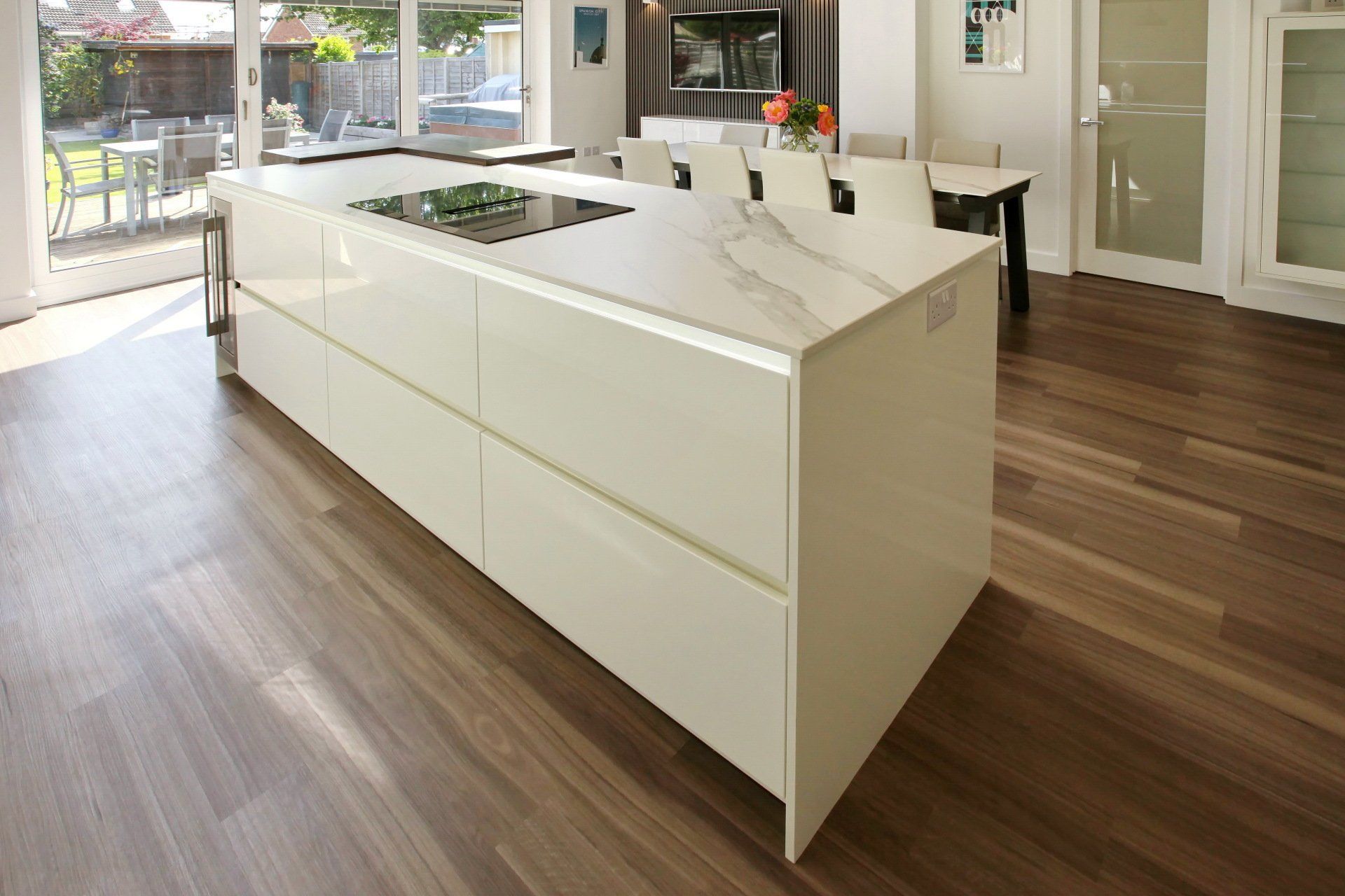 Modern kitchen island with white cabinets, cooktop, and wooden flooring.