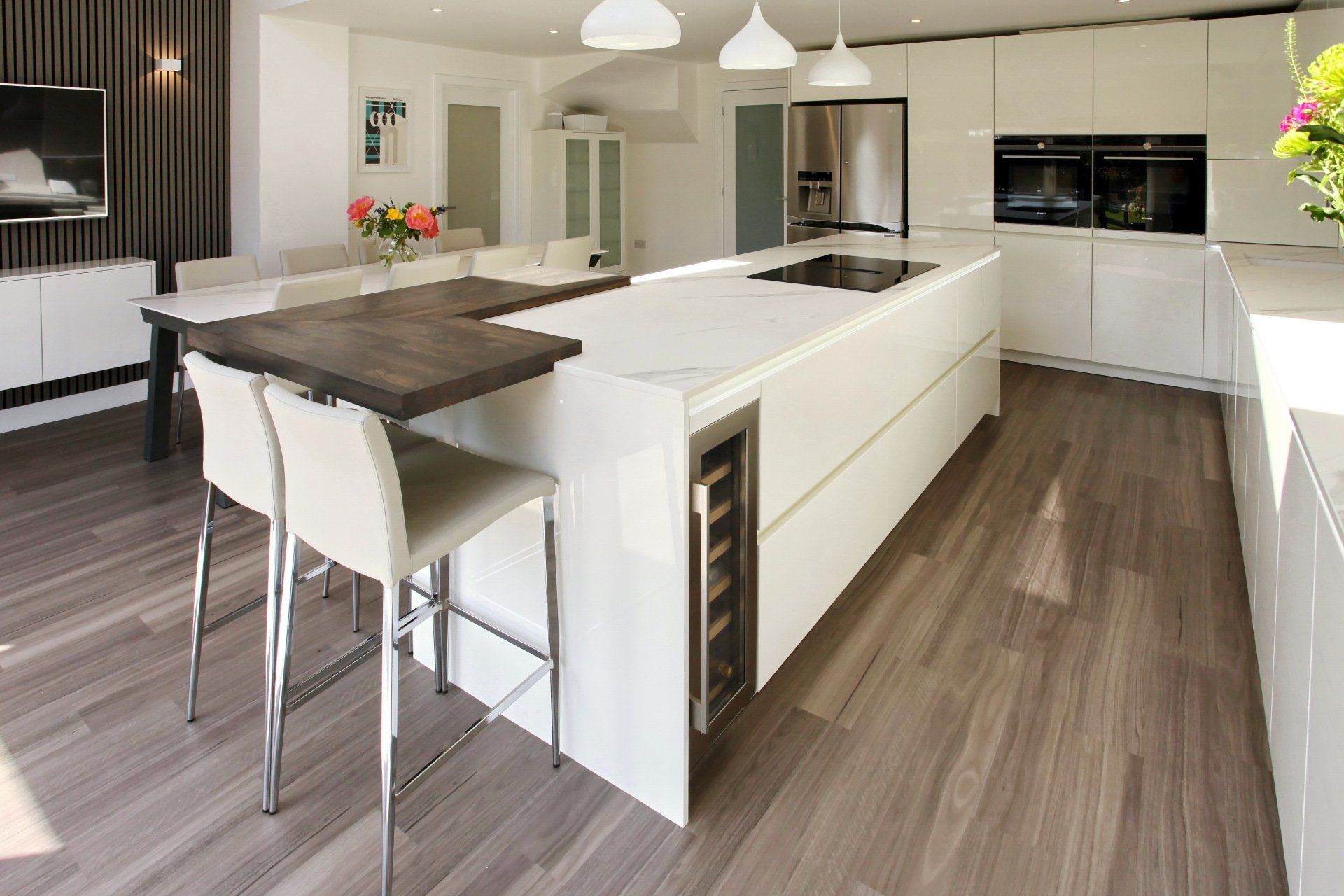Modern white kitchen with island, wooden countertop, bar stools, and built-in wine cooler.