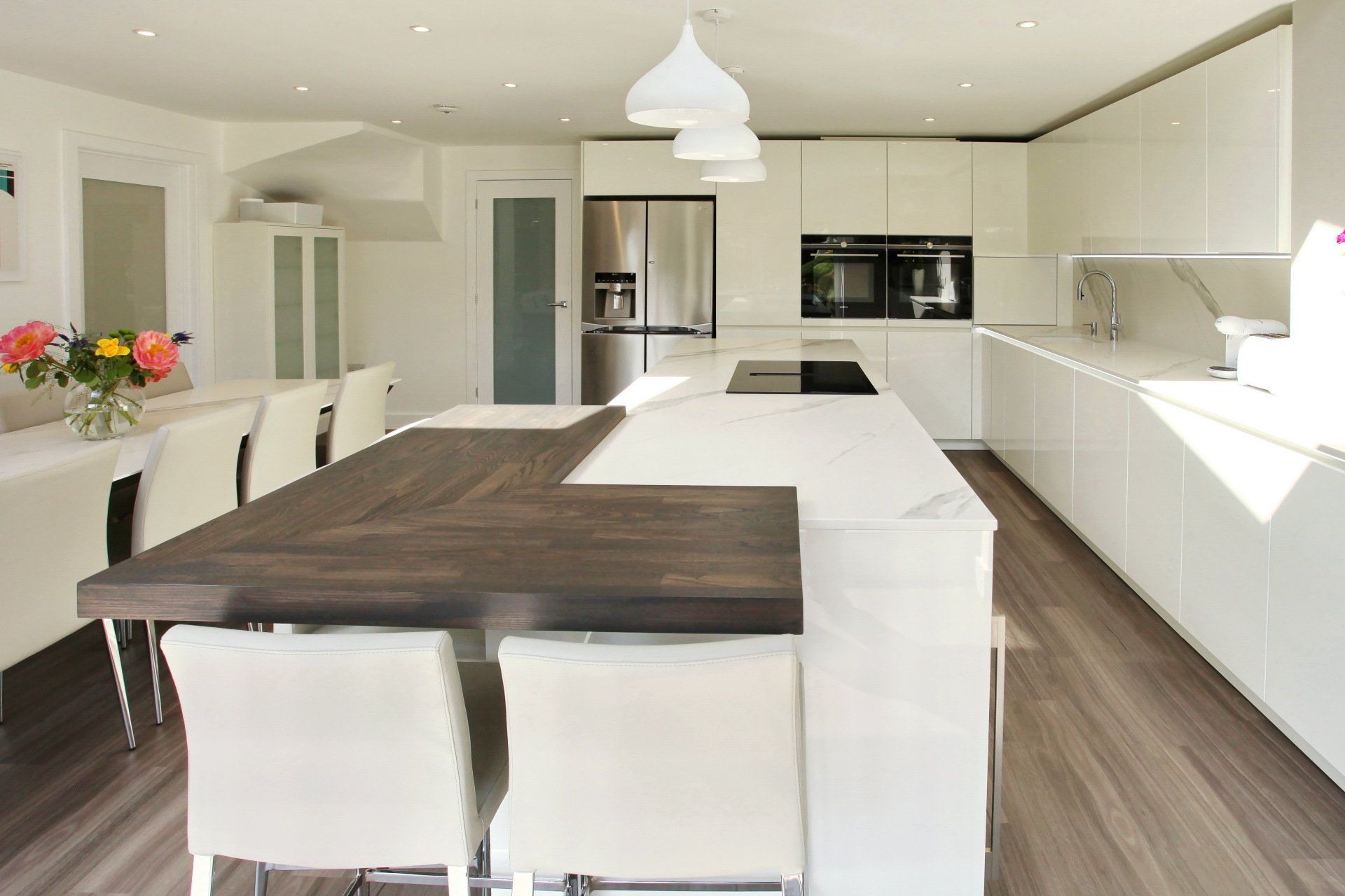 Modern white kitchen with island and dark wooden countertop, dining table with flowers.
