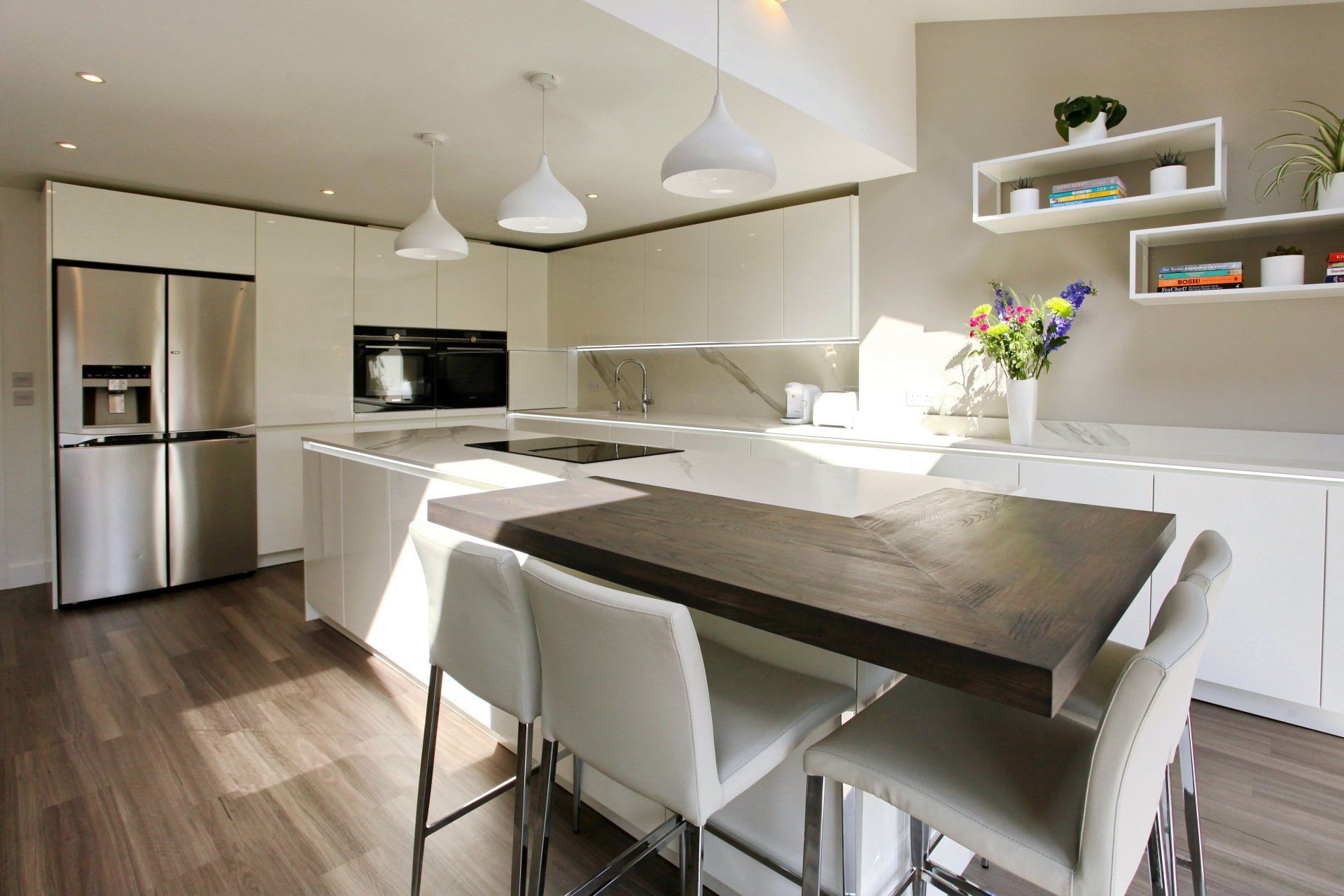 Modern white kitchen with stainless steel appliances, island seating, and wood floors.