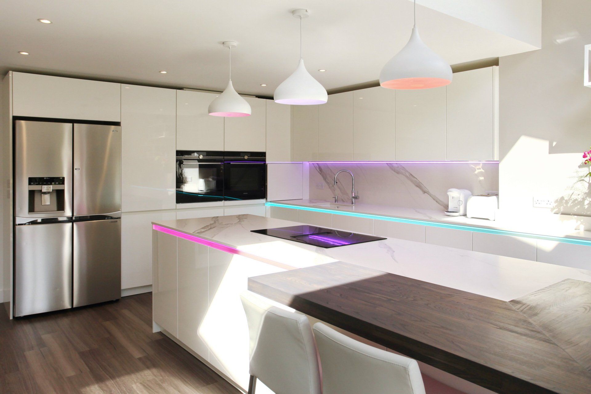 Modern white kitchen with stainless steel appliances, island, and colorful LED lighting.