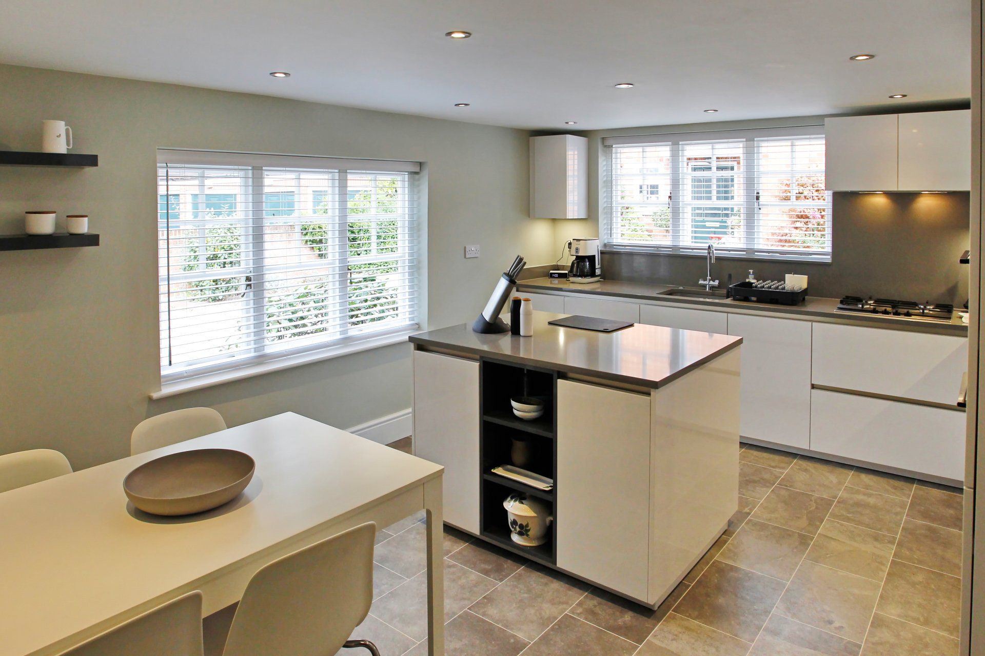 Modern kitchen with white cabinets, island, table, and large window with blinds.