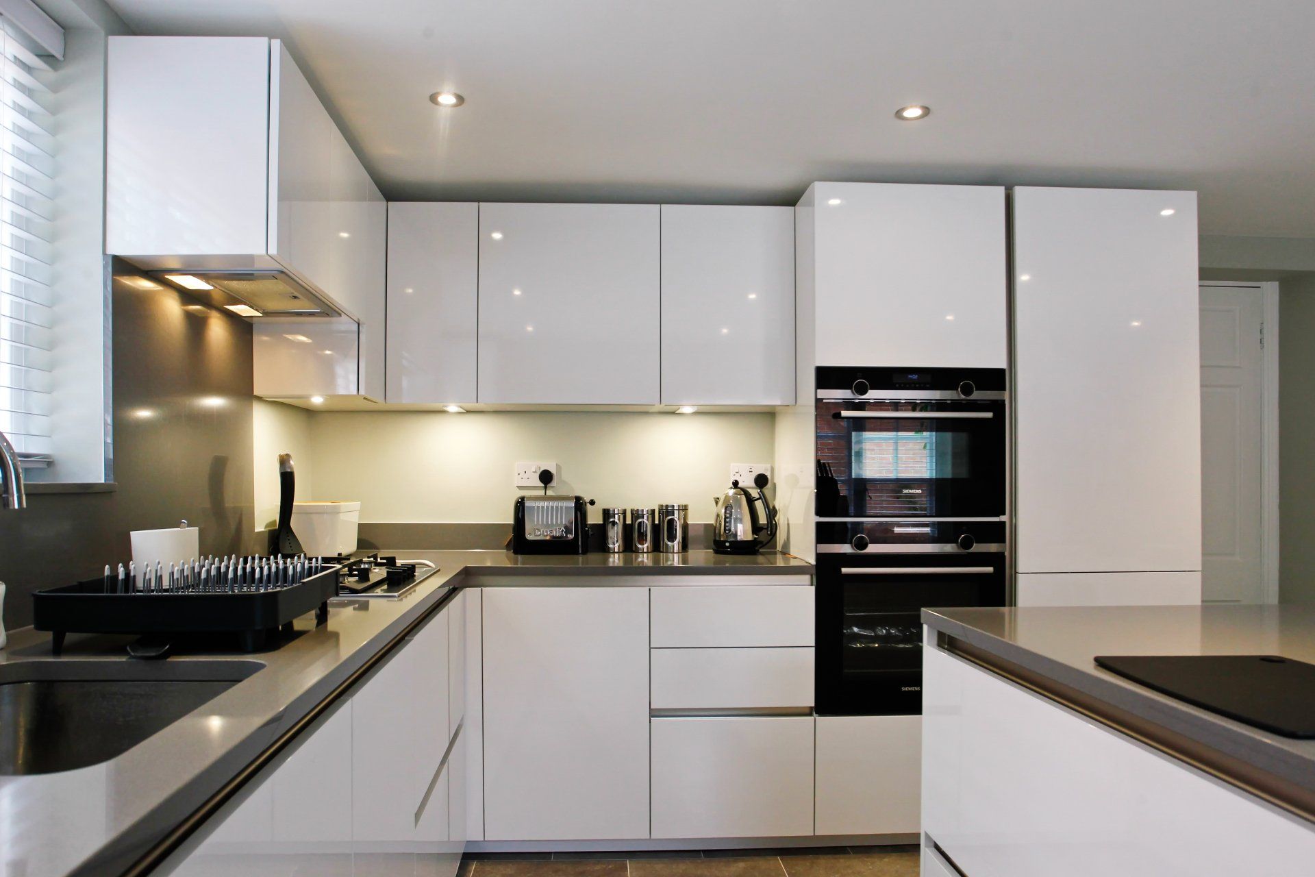Modern white kitchen with glossy cabinets, stainless steel countertops and appliances.