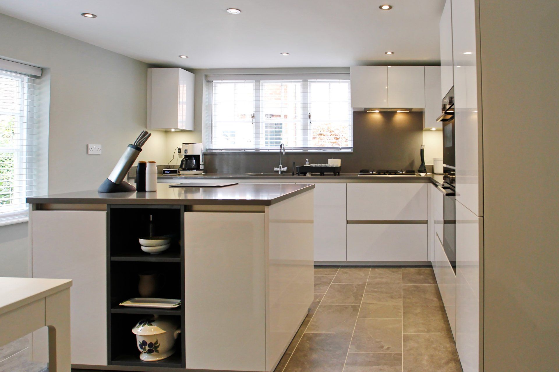 Modern white kitchen with island, gray countertop, built-in appliances, and tile floor.