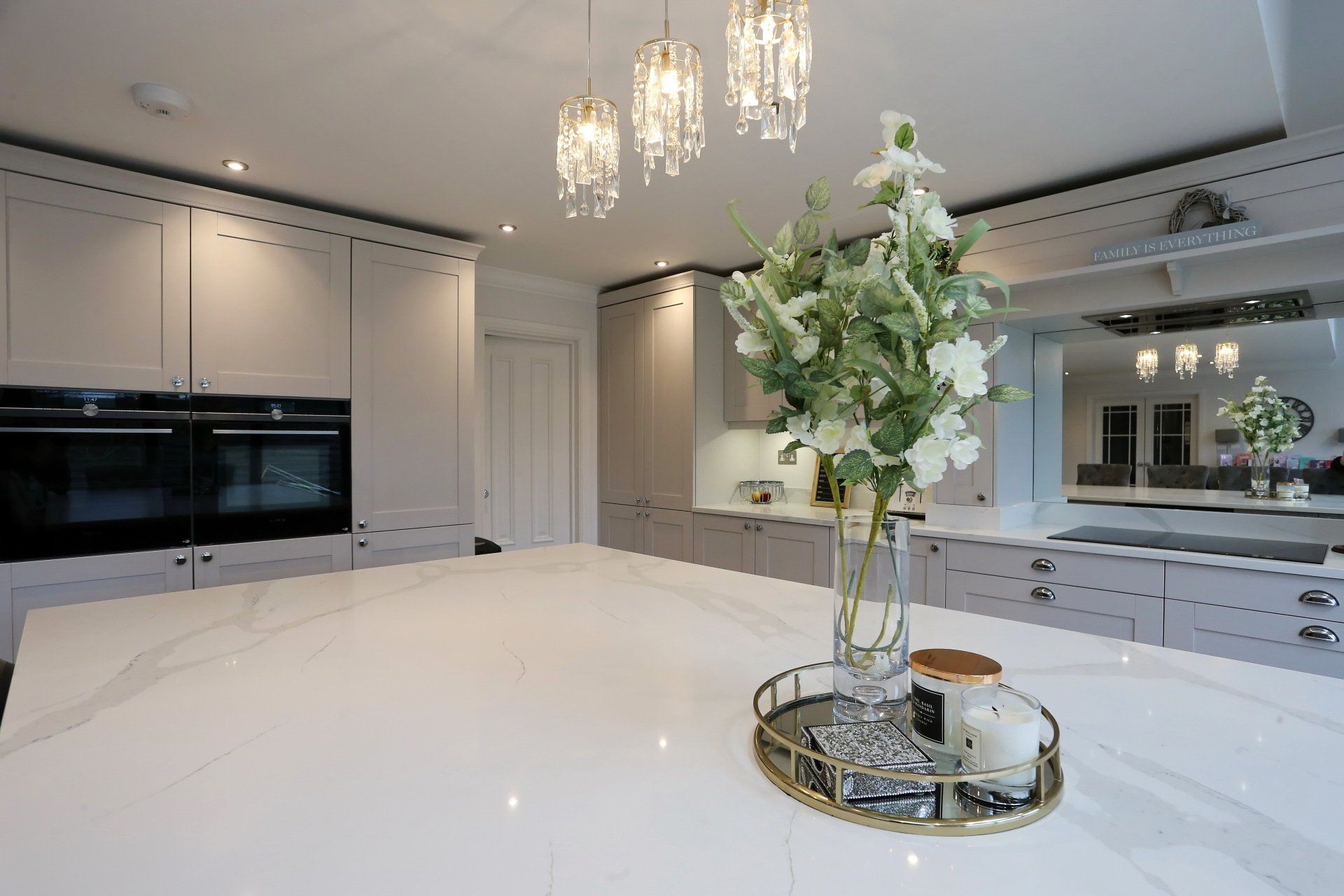 Elegant kitchen with white island, cabinets, chandelier, and a bouquet of flowers on a tray.