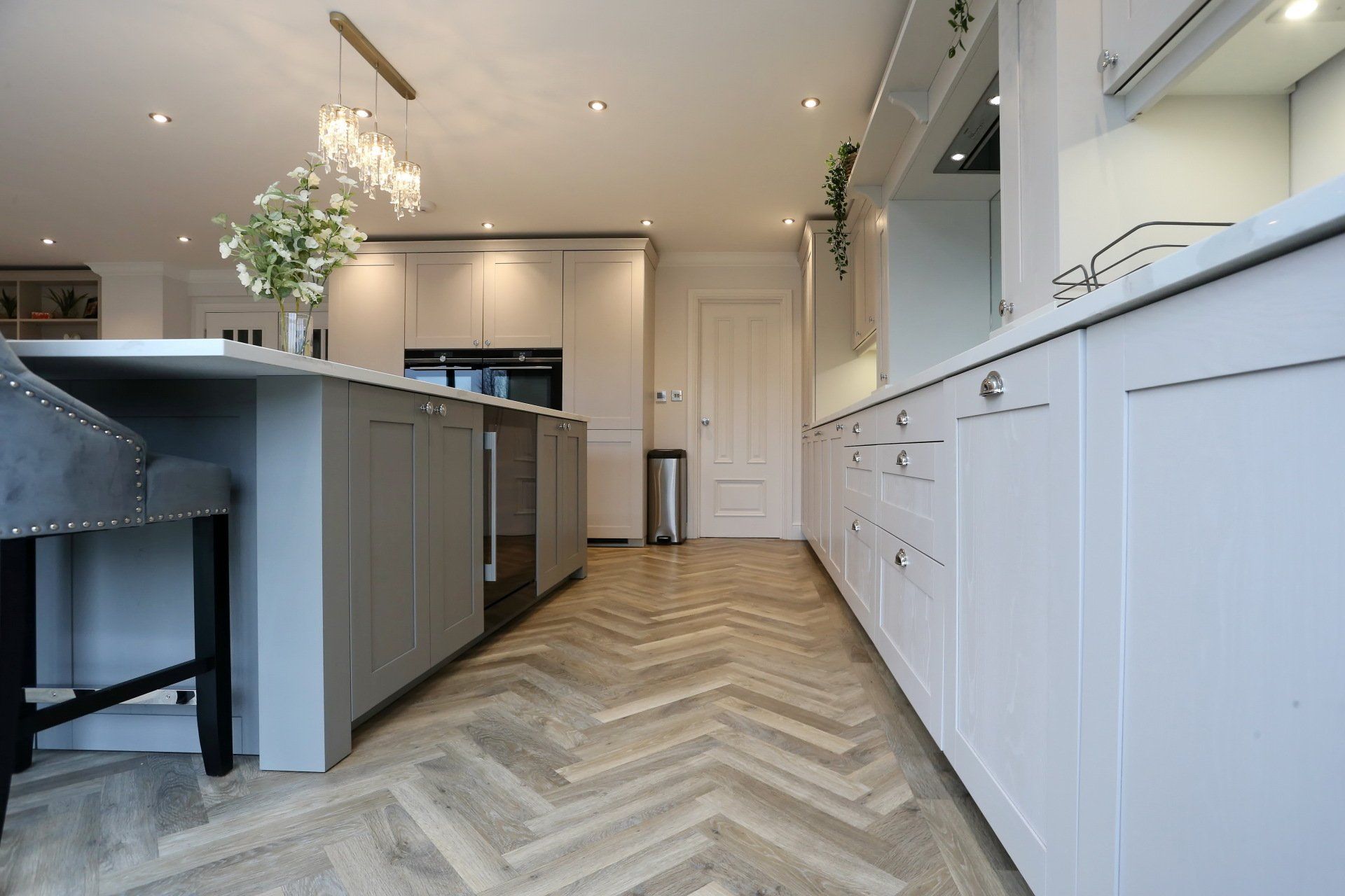 Gray and white kitchen with herringbone wood floor, island, and cabinets.
