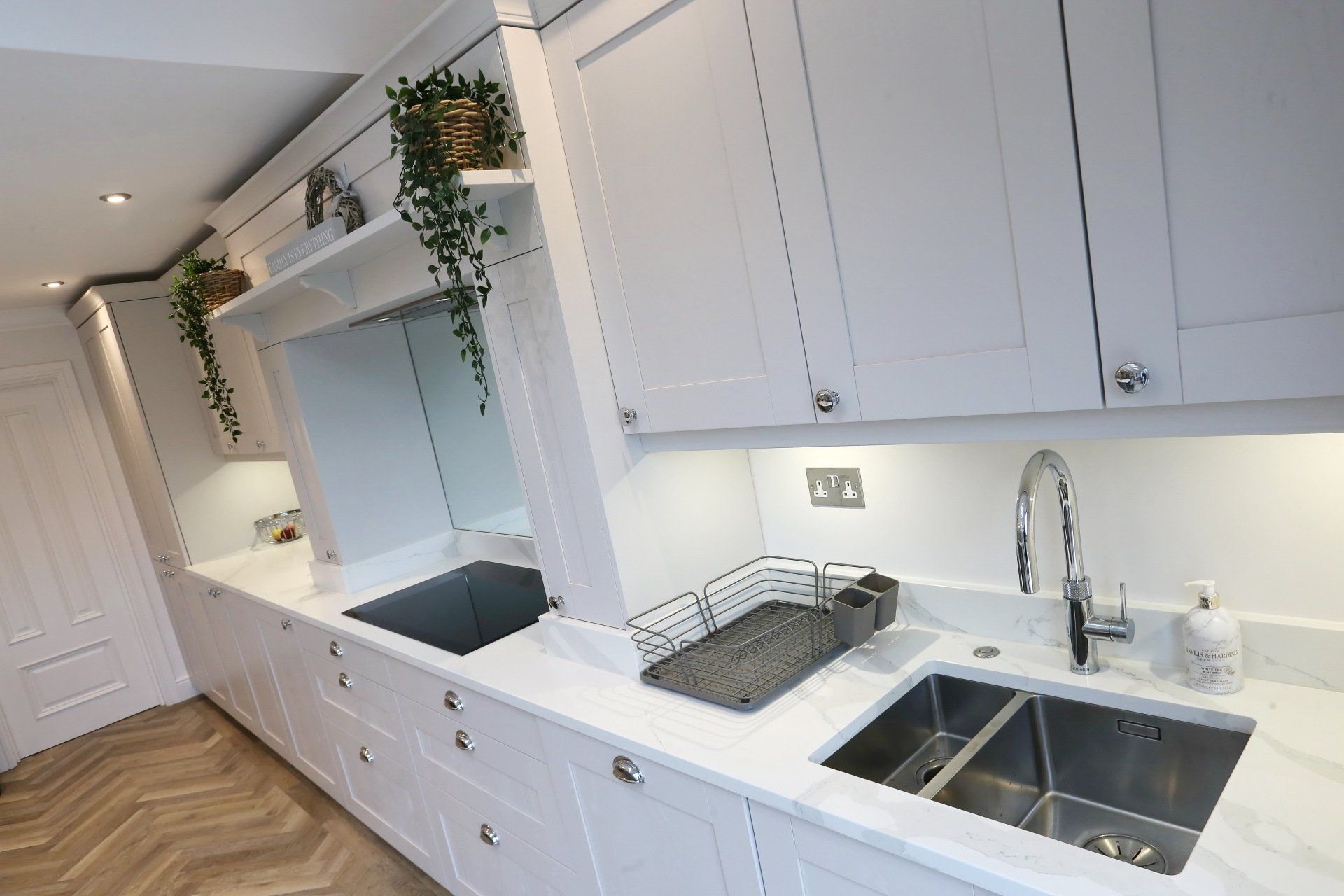 White kitchen with cabinets, sink, and countertop. Dish drying rack and faucet are visible.