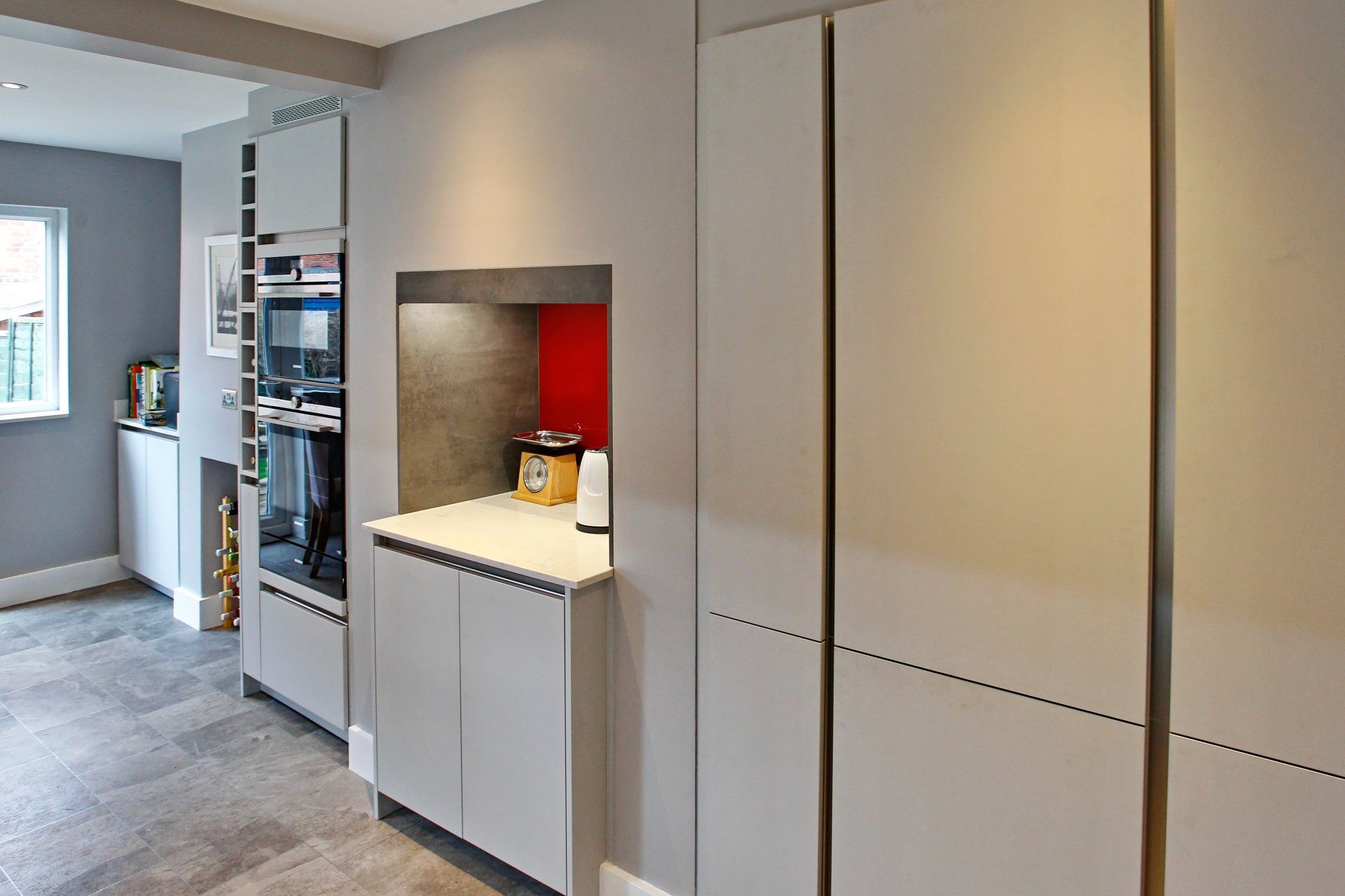 Modern gray kitchen with built-in appliances, recessed countertop, and red backsplash.