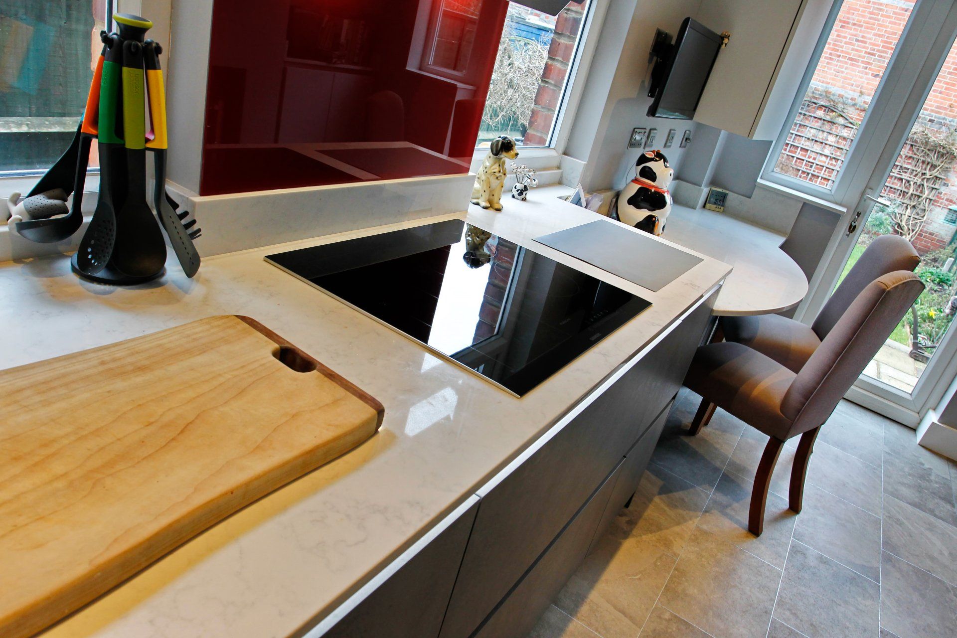Modern kitchen with cooktop, cutting board, and a red backsplash.