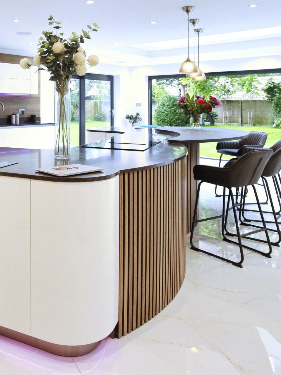 Modern kitchen island with white cabinets, wood paneling, and black countertop, with bar stools, and a round table.
