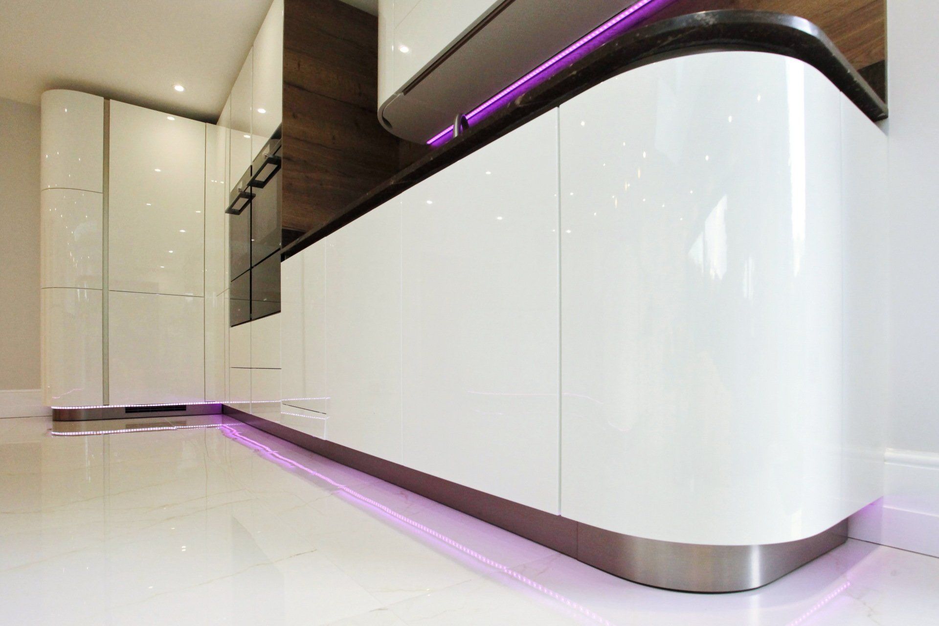 Modern white kitchen with curved glossy cabinets, accented by purple LED lighting.