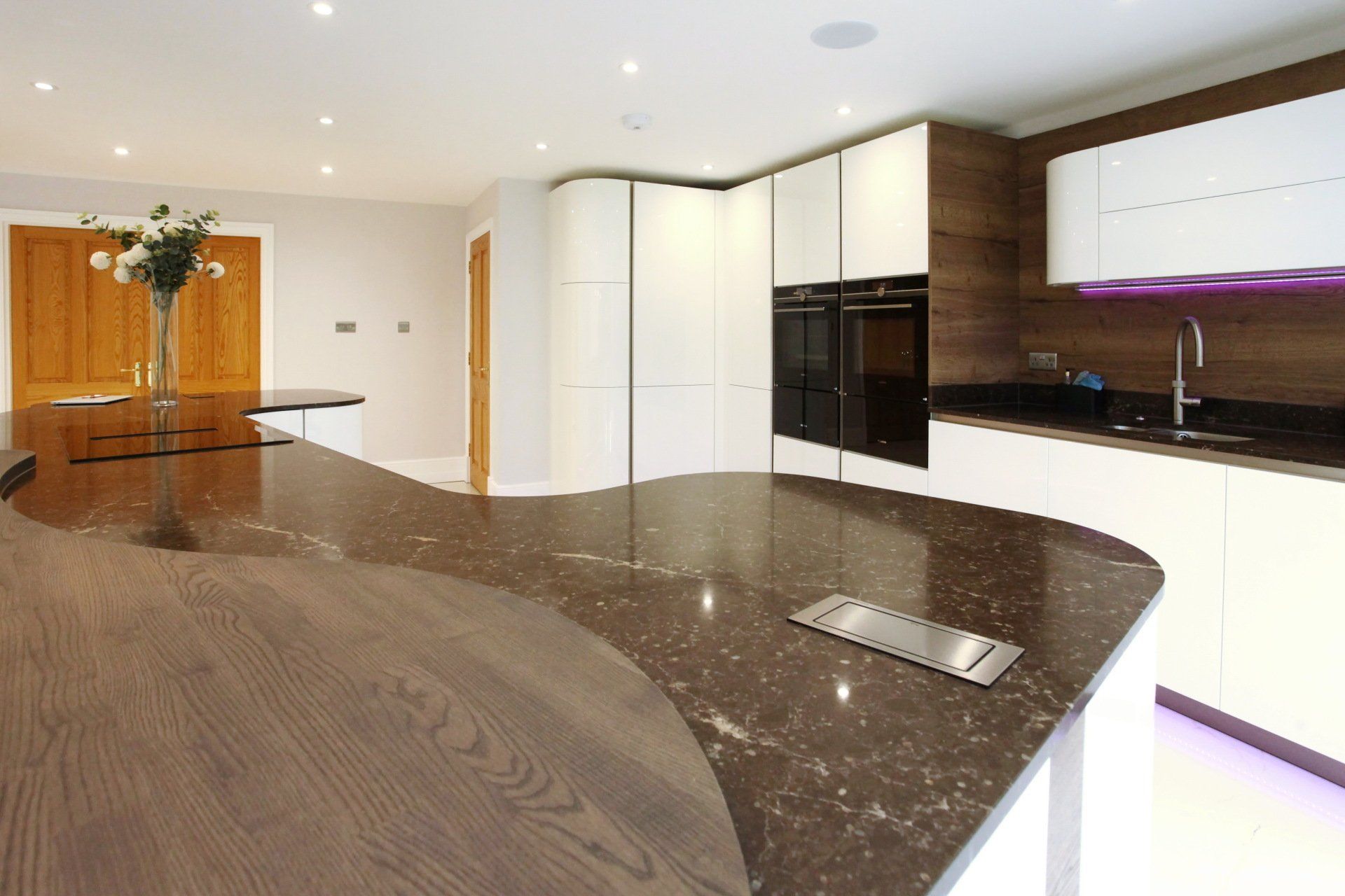 Modern kitchen with curved brown countertop, white cabinets, and built-in appliances.
