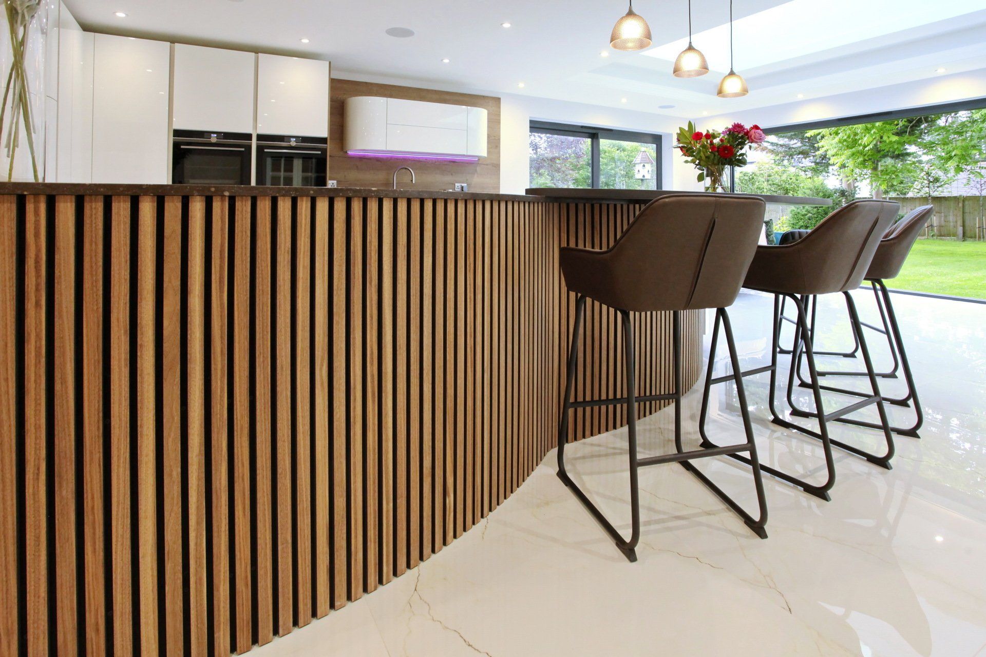Modern kitchen with wood slat bar, white cabinets, and bar stools.