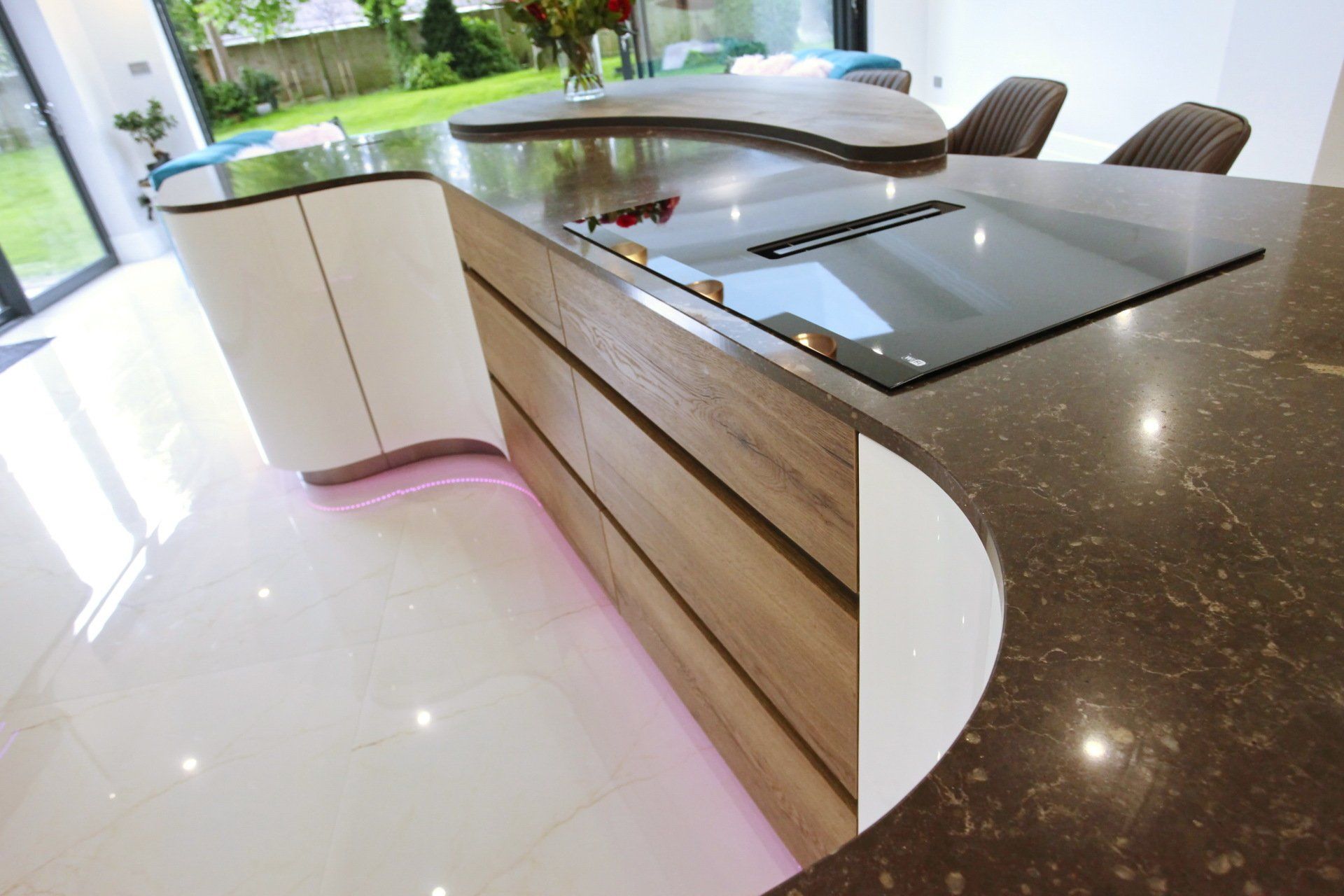 Modern kitchen island with dark countertop, built-in cooktop, and wooden drawers. White cabinets and flooring.