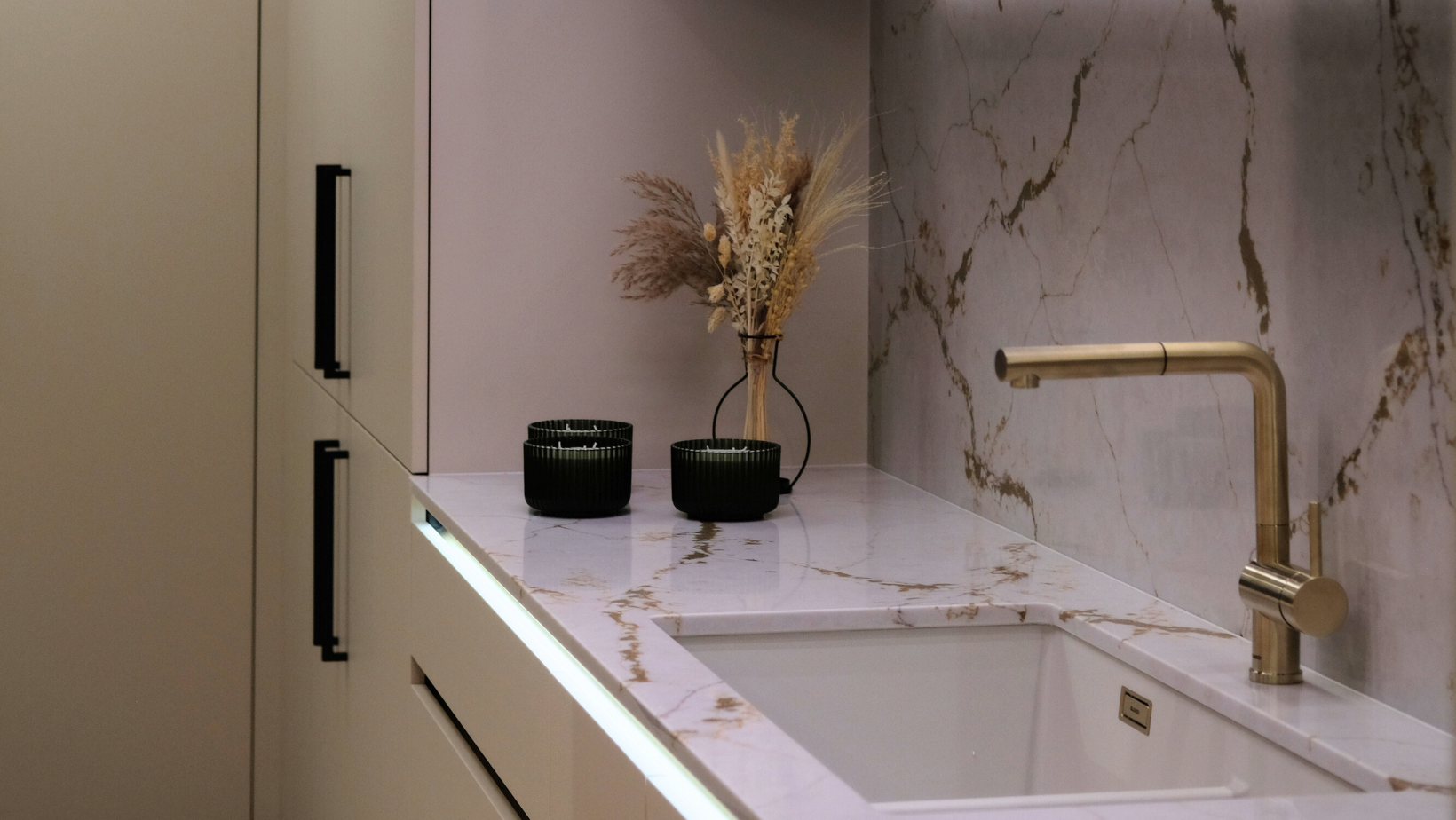 Modern kitchen sink with gold faucet, marble backsplash, and decorative elements.