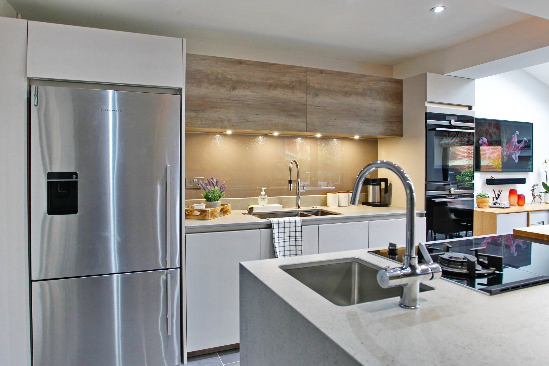 Modern kitchen with stainless steel refrigerator, white cabinets, light wood accent cabinets, and a central island with a sink.