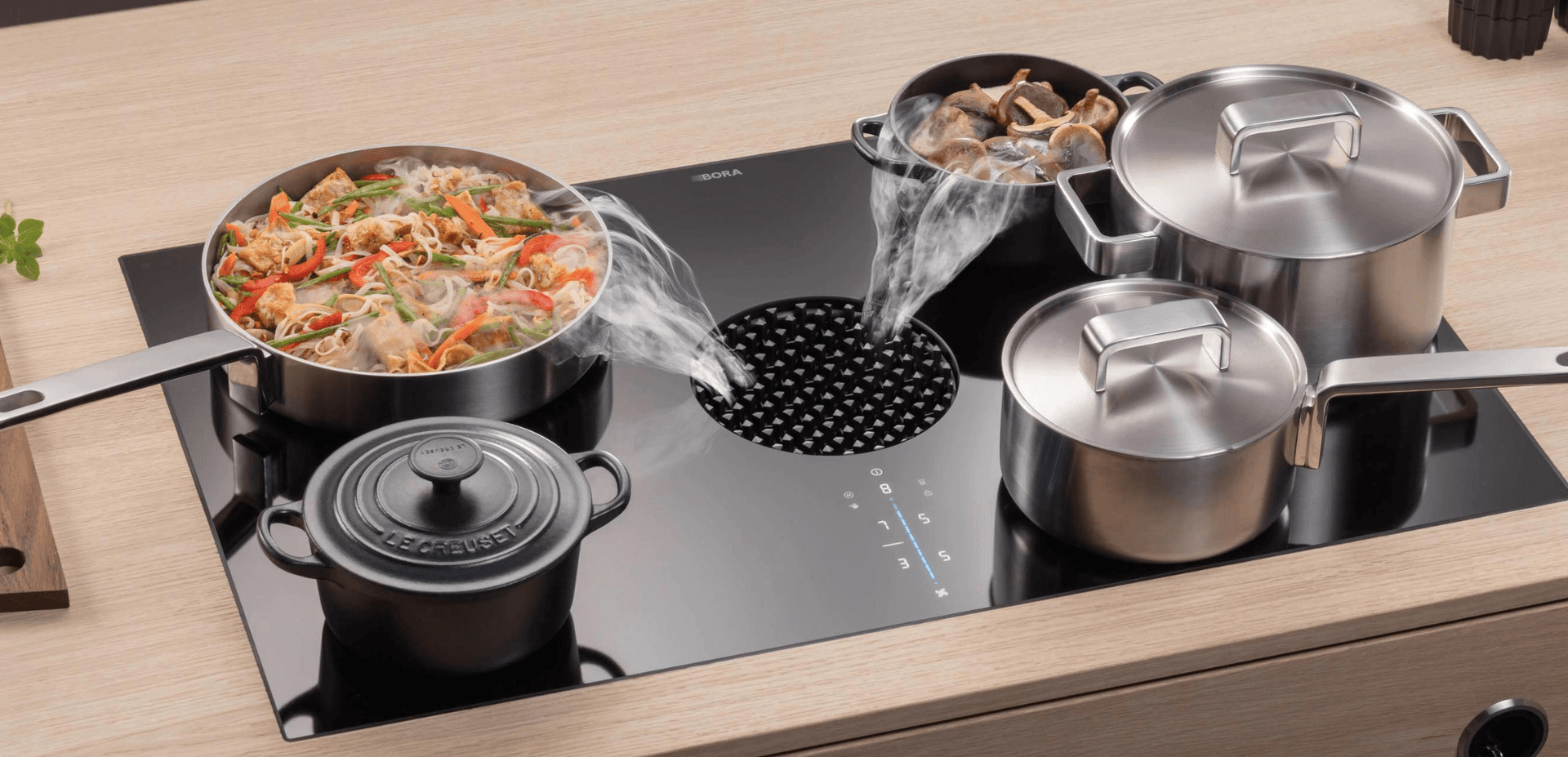 Kitchen stovetop with pots and pans steaming, and a built-in vent.