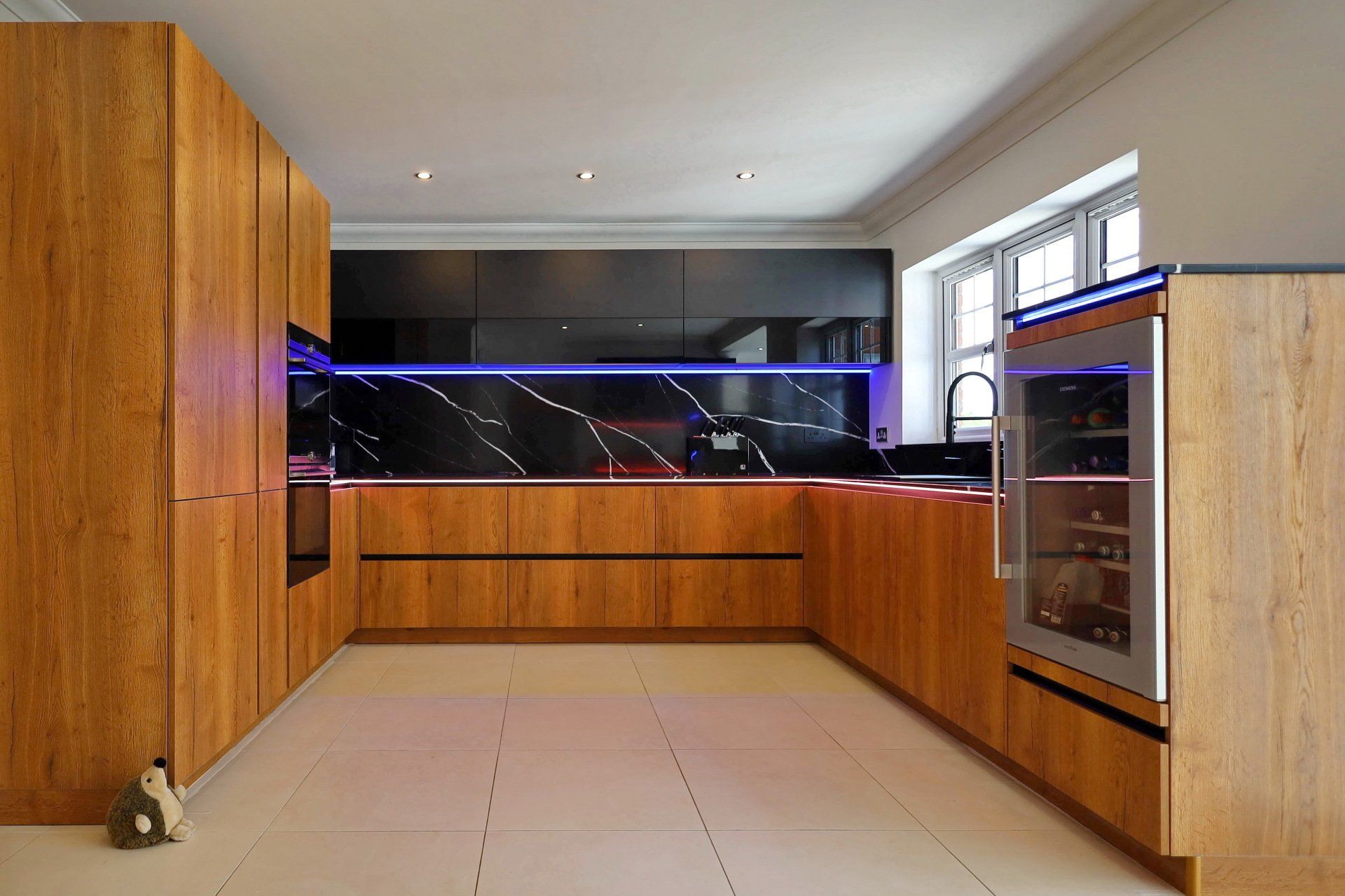 Modern kitchen with wood cabinets, black backsplash, wine fridge, and LED lighting.