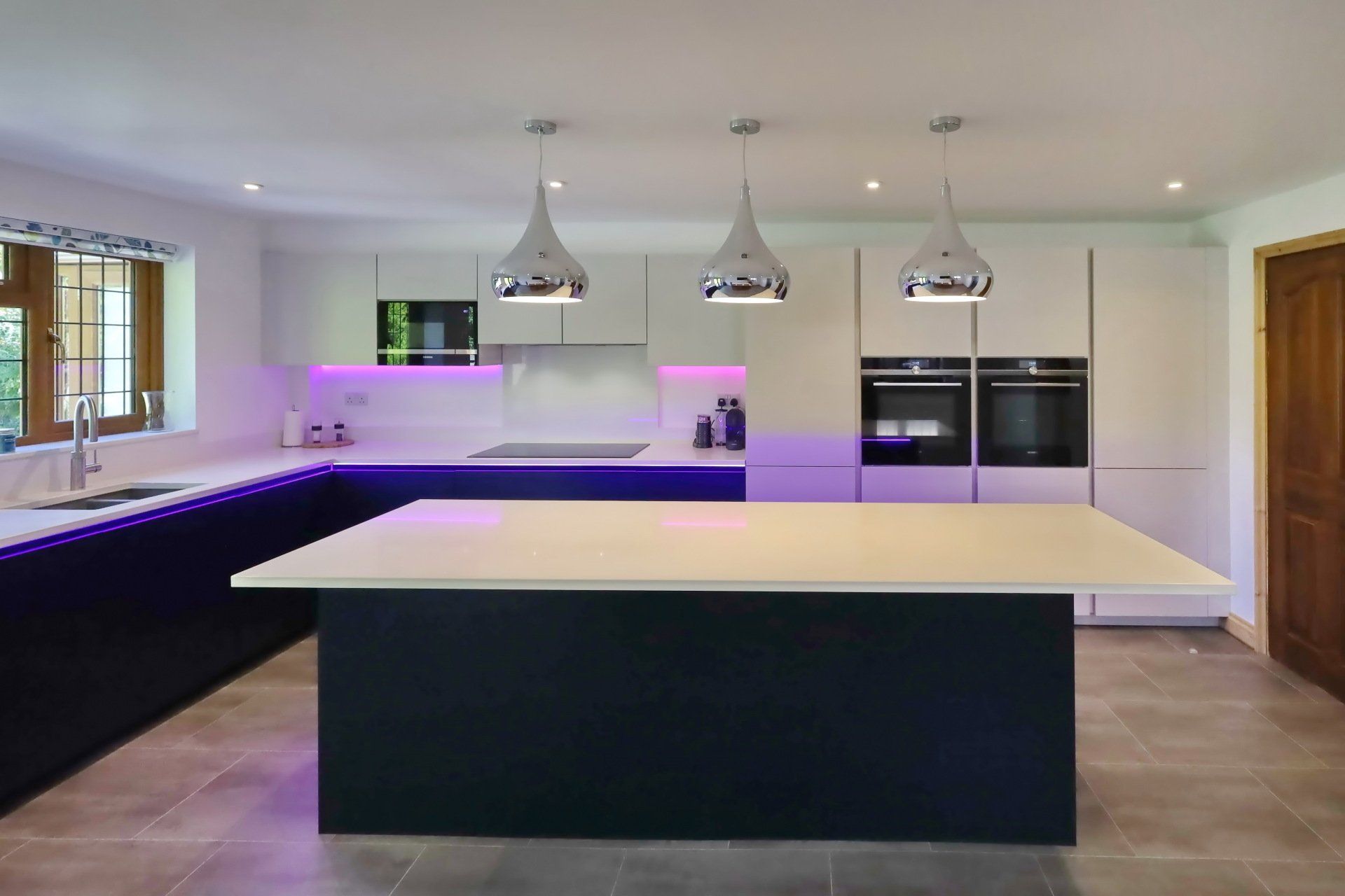 Modern kitchen with white cabinets, dark blue island, and chrome pendant lights.