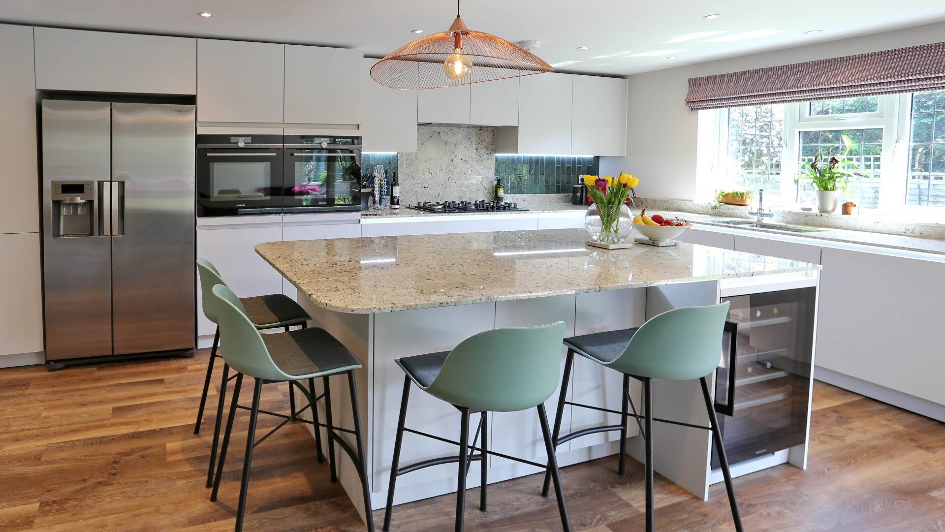 Modern white kitchen with a granite island, seating, and stainless steel appliances.