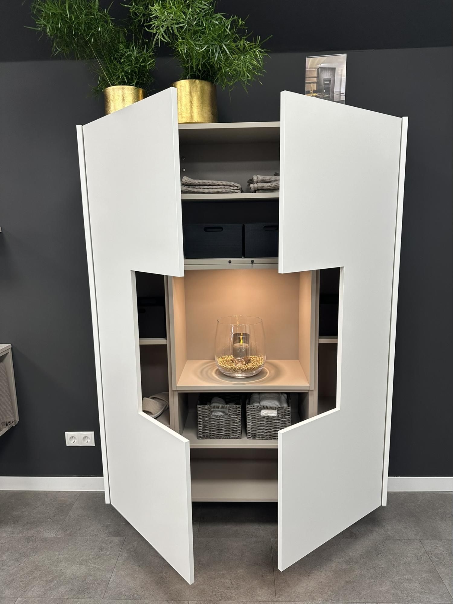 White cabinet with open doors, shelves, and display niche lit from within. Grey backdrop.