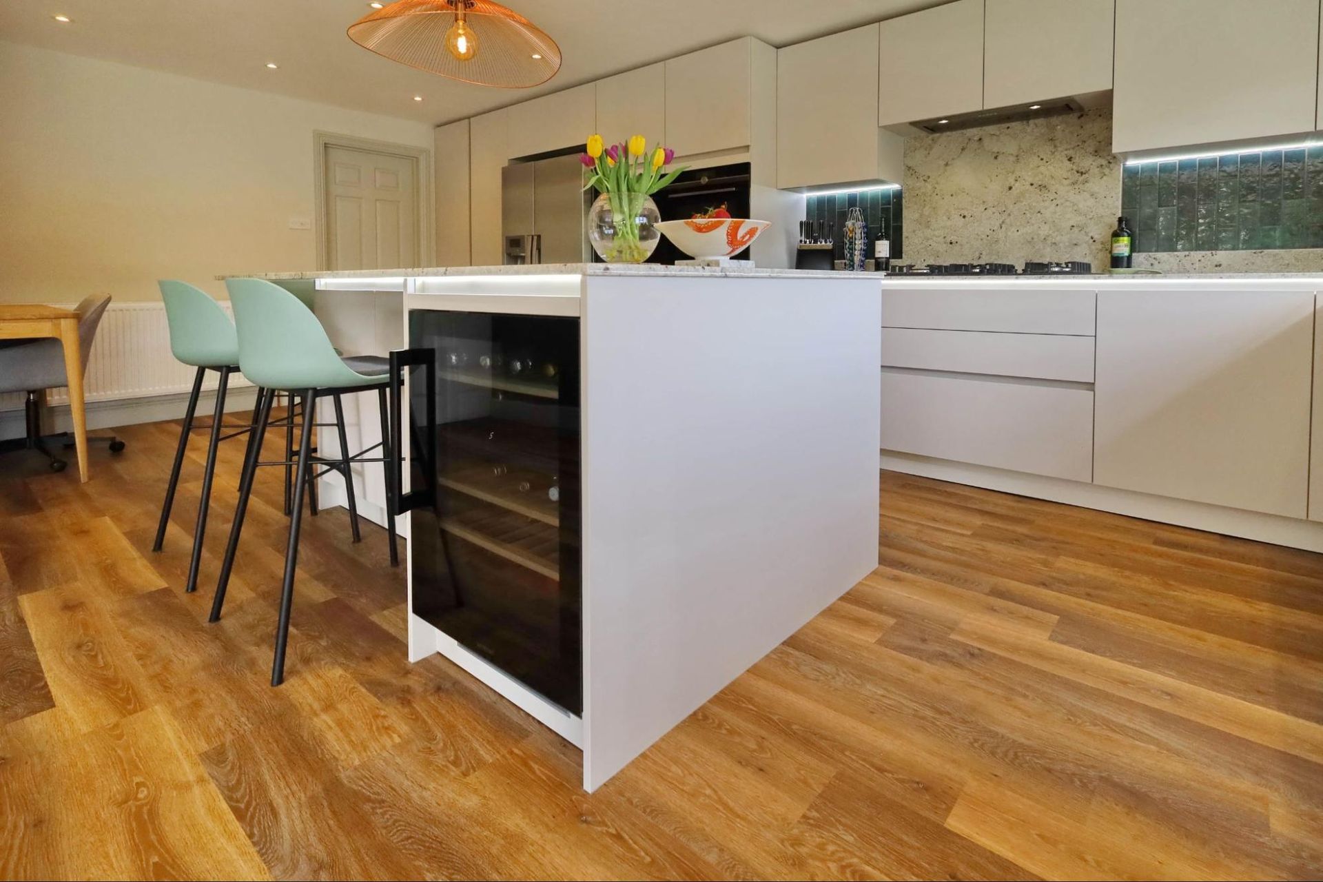 Modern kitchen with white cabinets, island with wine fridge, wood floor, and teal stools.