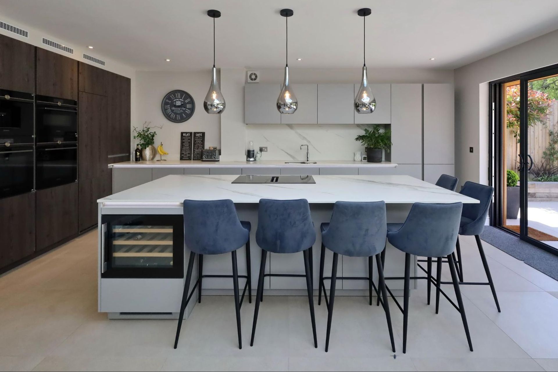 Modern kitchen with large island, gray cabinets, wine fridge, and blue bar stools.