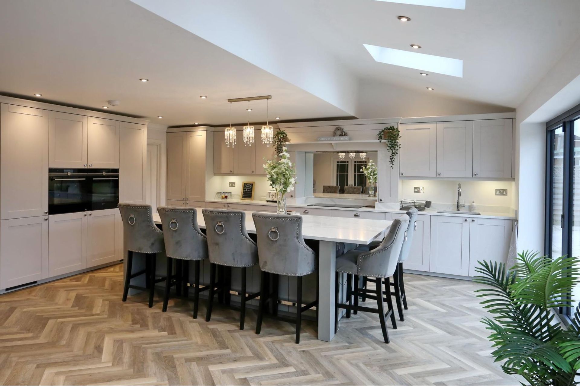 Spacious modern kitchen with island seating, pale cabinetry, herringbone floors, and skylights.