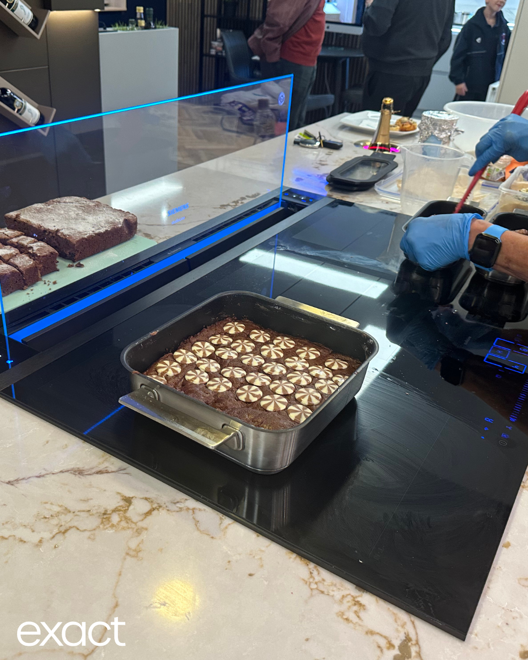 A square pan of brownies with flower decorations on a black stovetop, next to a cutting board with more brownies.