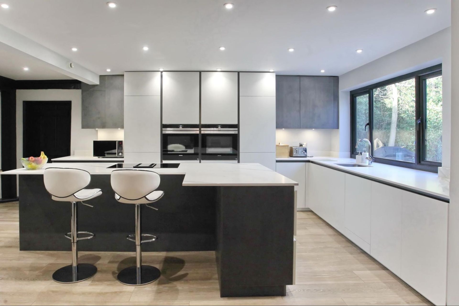 Modern kitchen with a black island, white countertops, and light wood flooring.