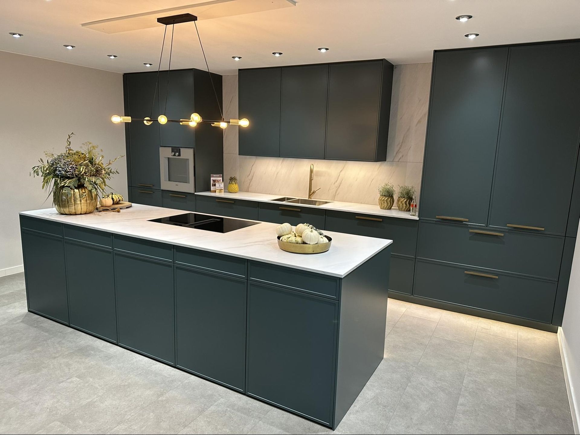 Modern teal kitchen with white countertops and gold fixtures.