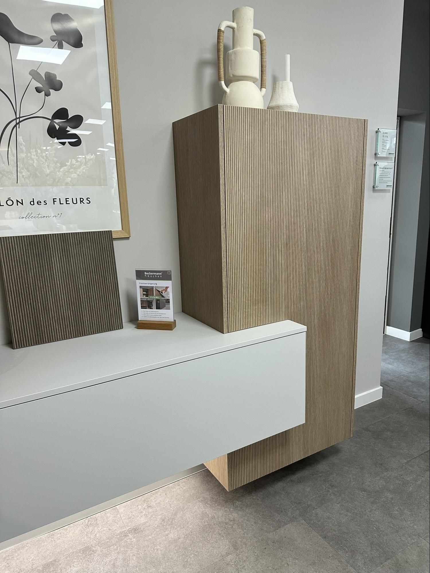 A modern display featuring textured wood cabinet with vases, artwork and white shelf in a showroom.