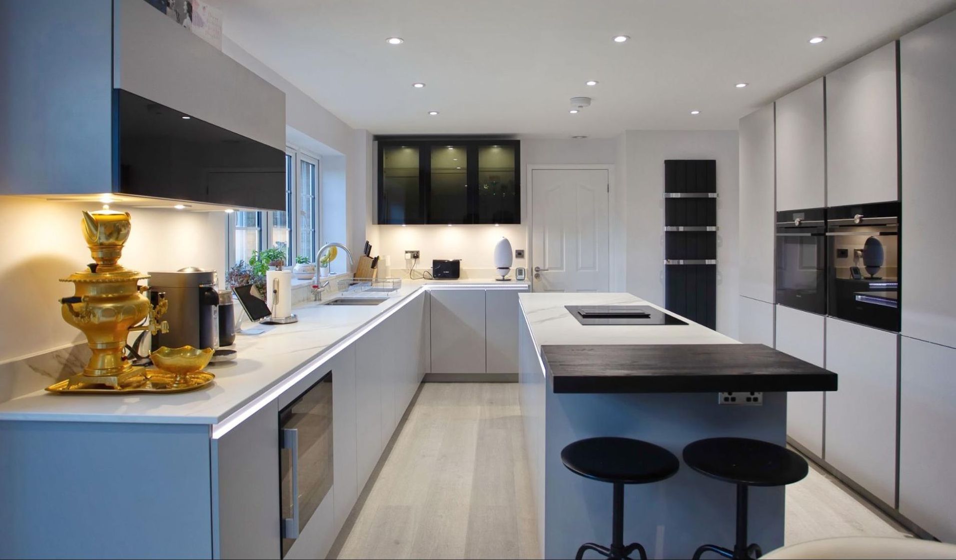 Modern, U-shaped kitchen with gray cabinets, white countertops, and a black island with two bar stools.