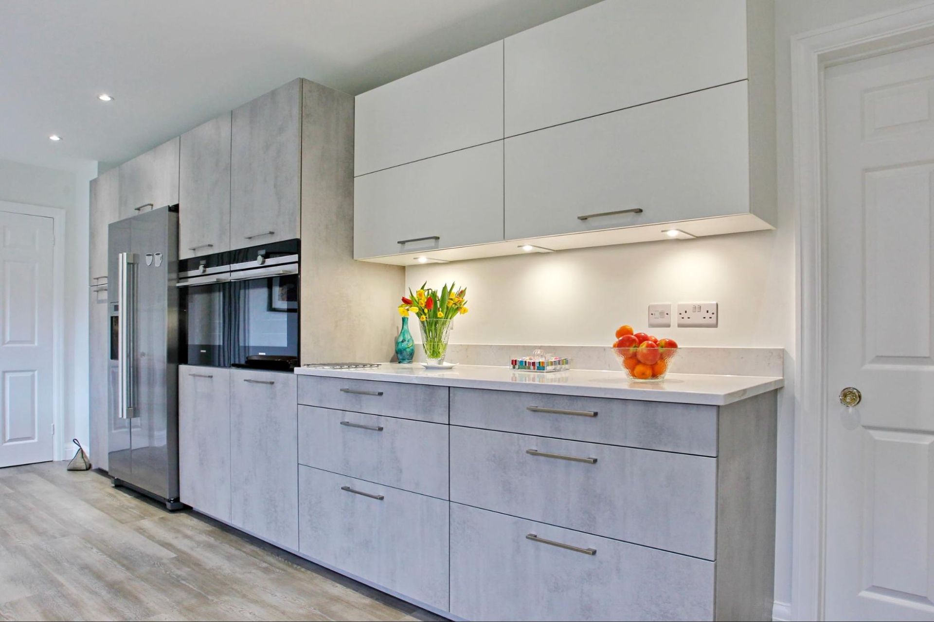 Modern kitchen with light grey and white cabinets, stainless steel appliances, and countertop lighting.