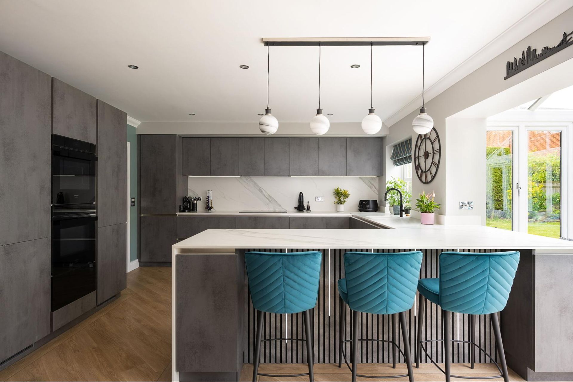 Modern gray kitchen with teal bar stools, white countertops, and globe pendant lights.