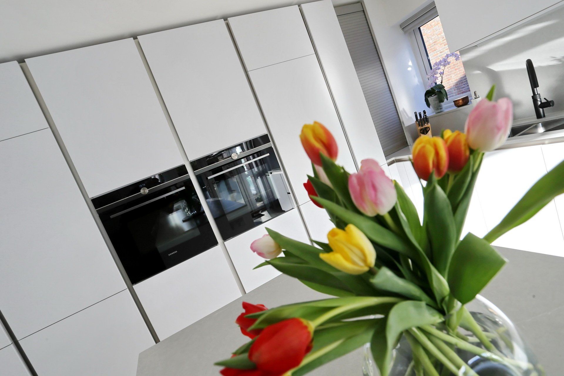 Bouquet of colorful tulips in a glass vase on a white kitchen countertop with built-in ovens.