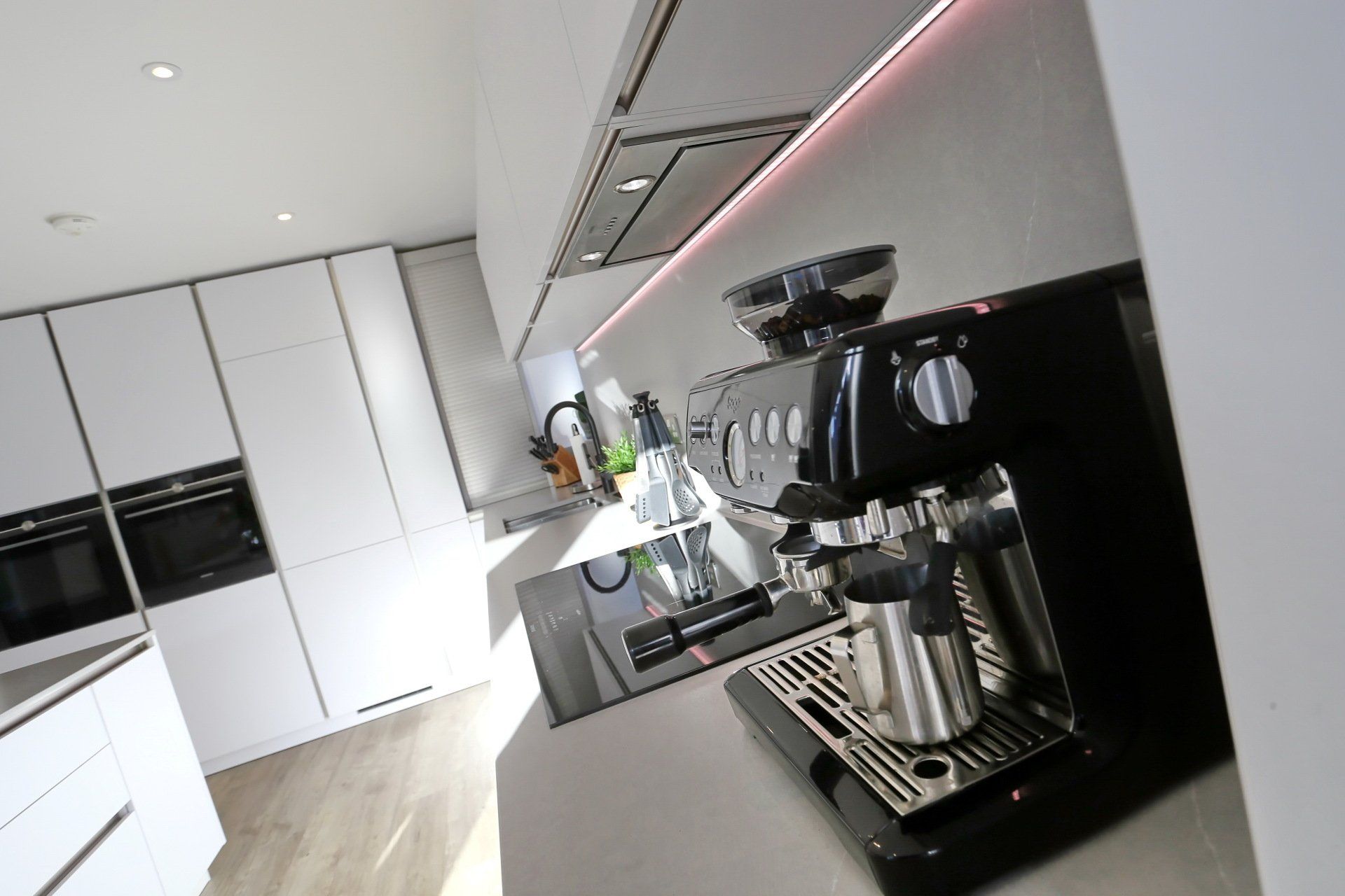 Black espresso machine on a white kitchen counter, with cabinets and lights in background.