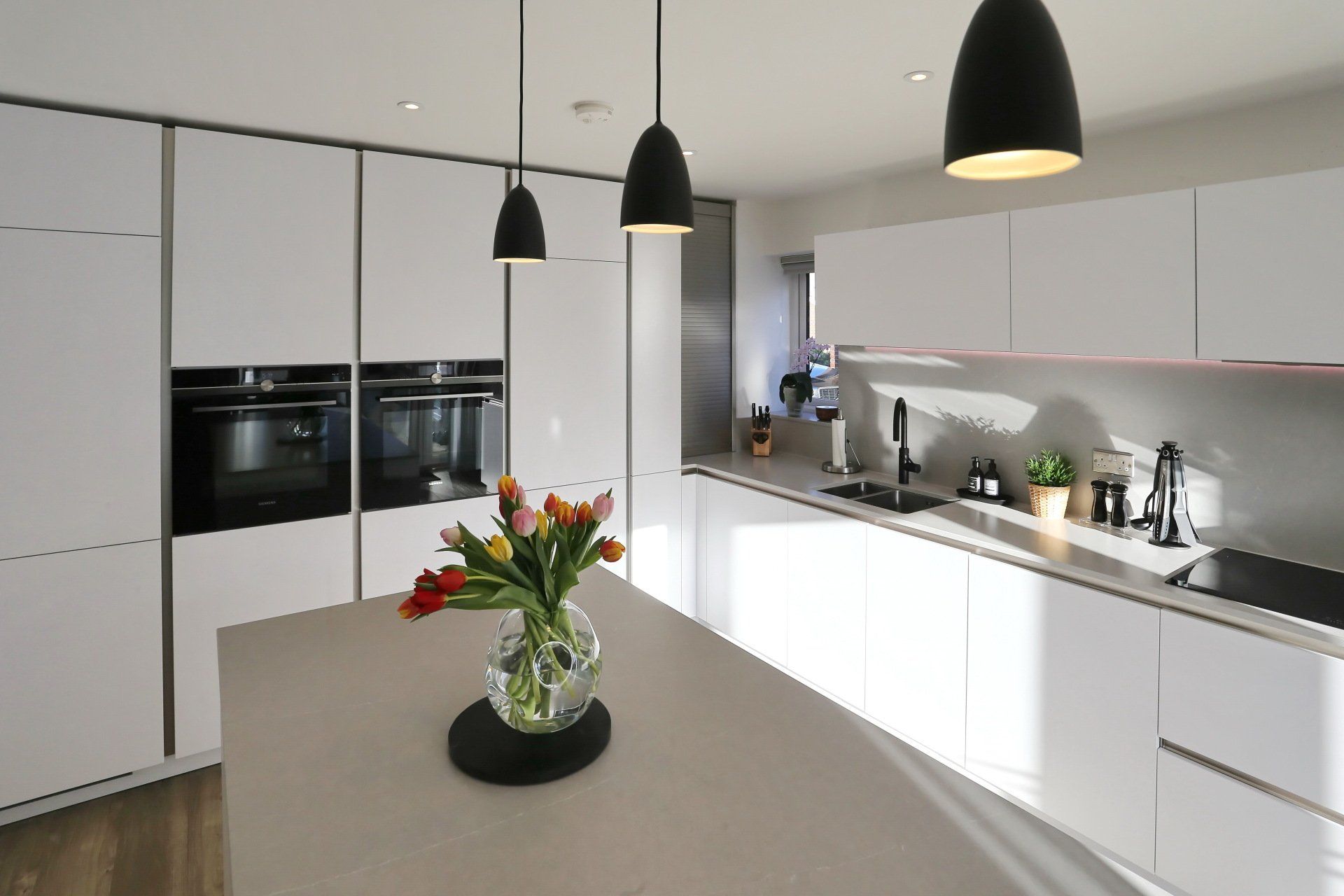 Modern white kitchen with island, black pendant lights, and tulips in vase.