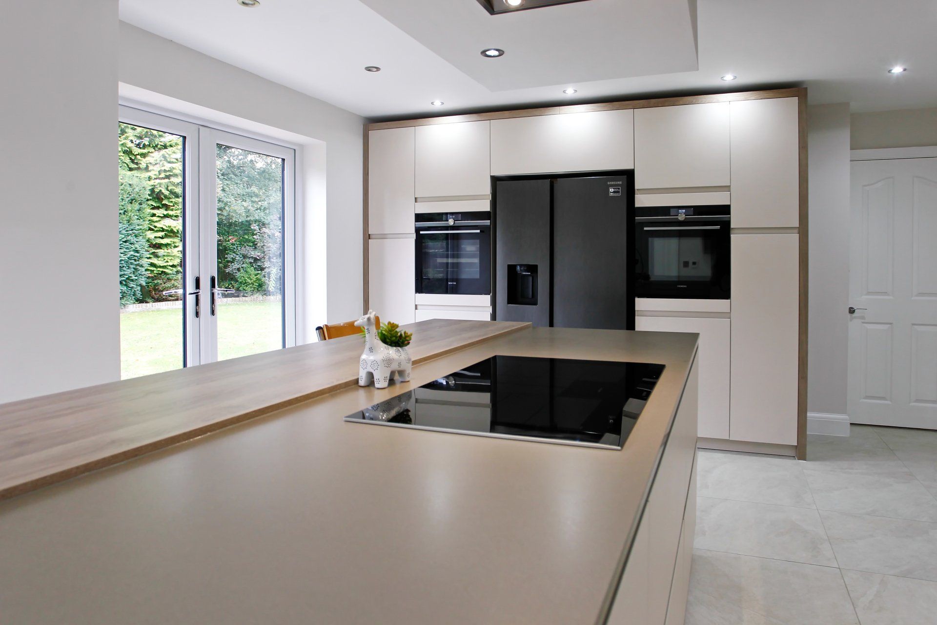 Modern kitchen with an island, cabinets, oven, and refrigerator. Light wood countertops and flooring. French doors.