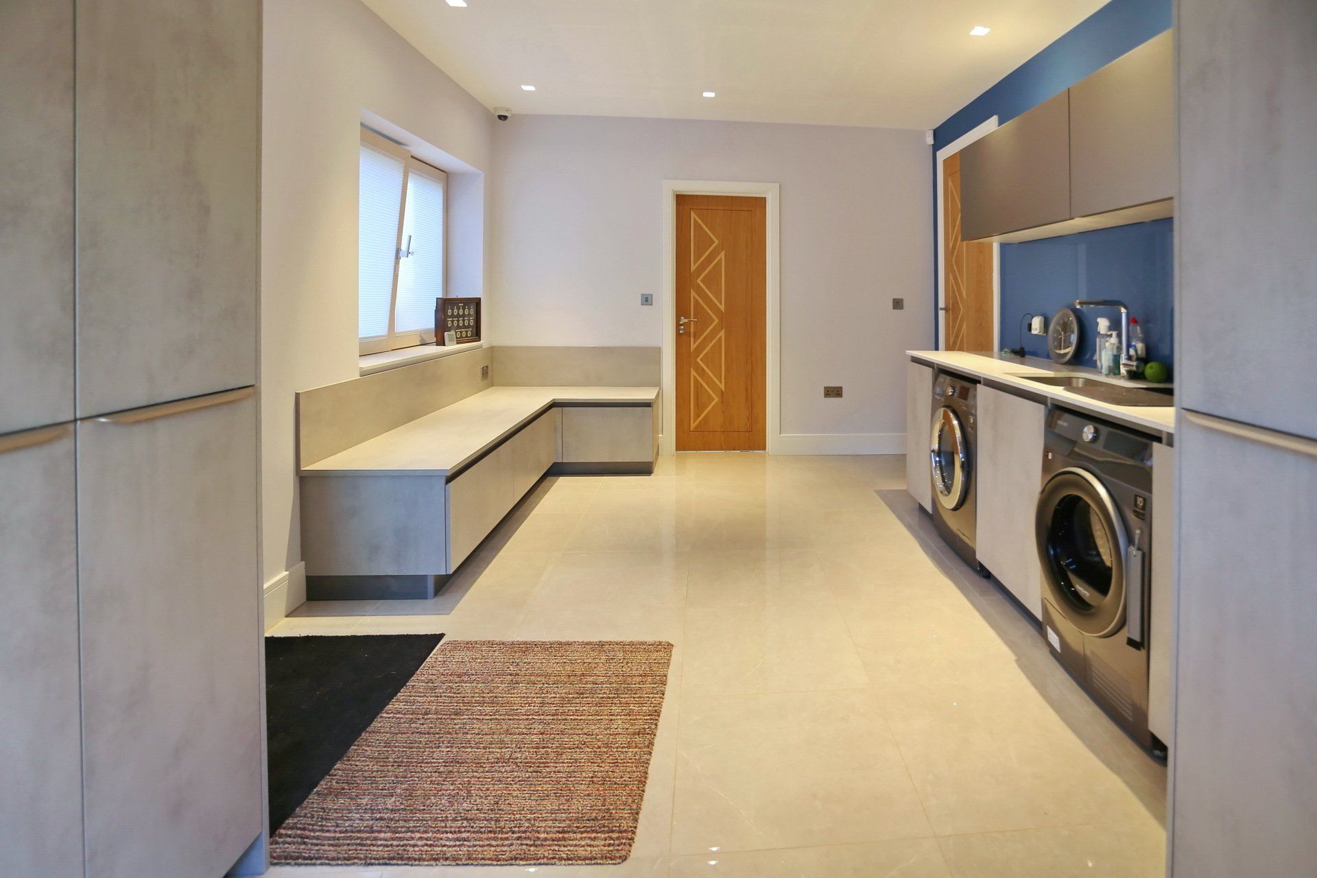 Modern laundry room with light gray cabinetry, built-in bench, washing machine, and neutral floors.
