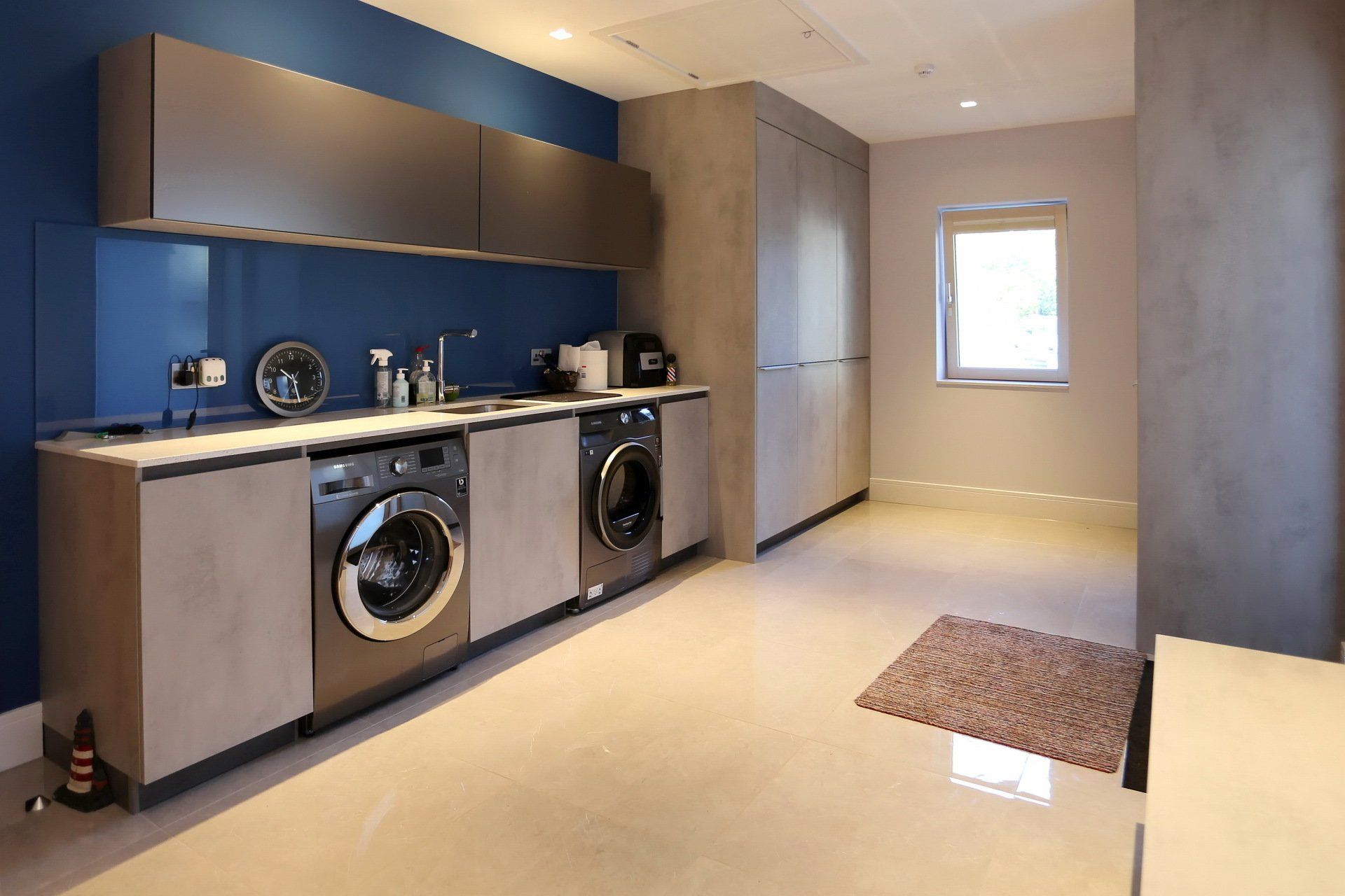 Laundry room with washer, dryer, cabinets, and a blue backsplash.