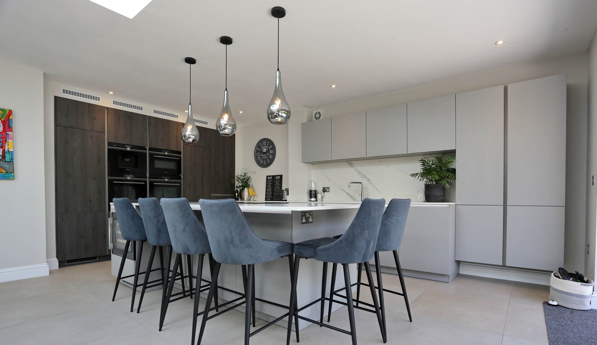 Modern kitchen with island, gray cabinets, blue bar stools, pendant lights, and dark wood cabinets.