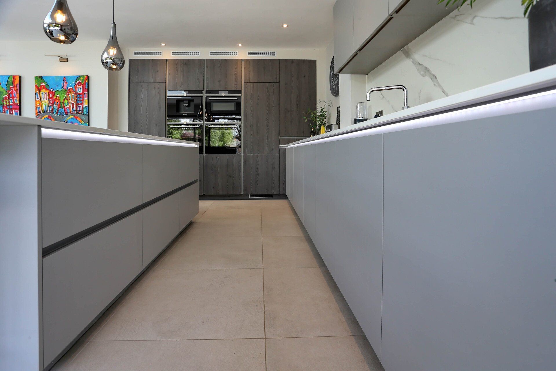 Modern kitchen with two light gray islands, dark gray cabinets, and built-in appliances.
