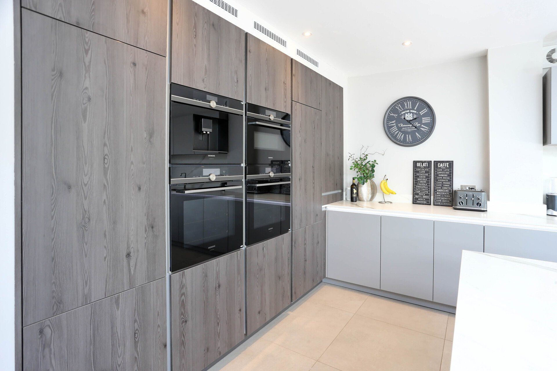 Modern kitchen with gray wood grain cabinets, built-in ovens, and a gray countertop.