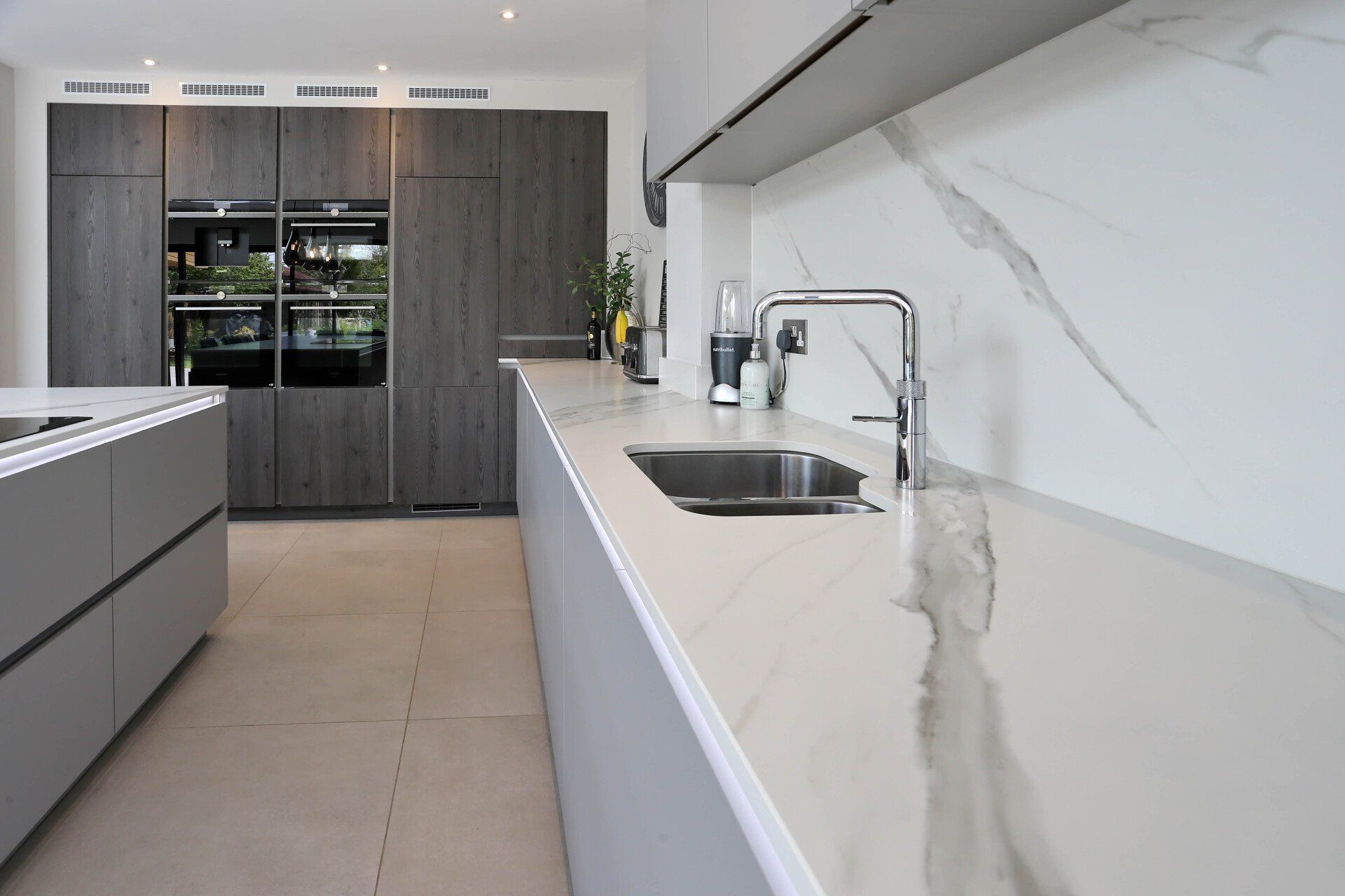 Modern kitchen with gray cabinets and white marble countertops.