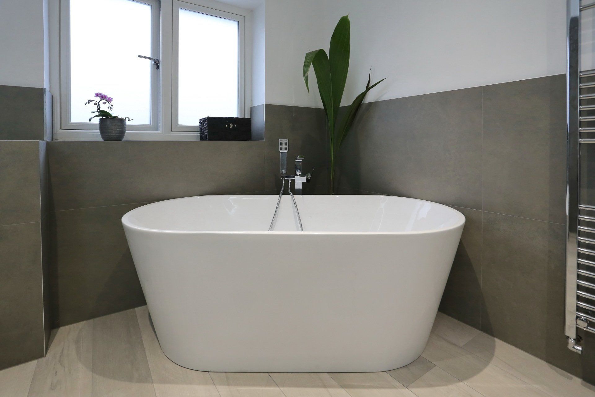 Modern bathroom with white freestanding tub, gray walls, and window.