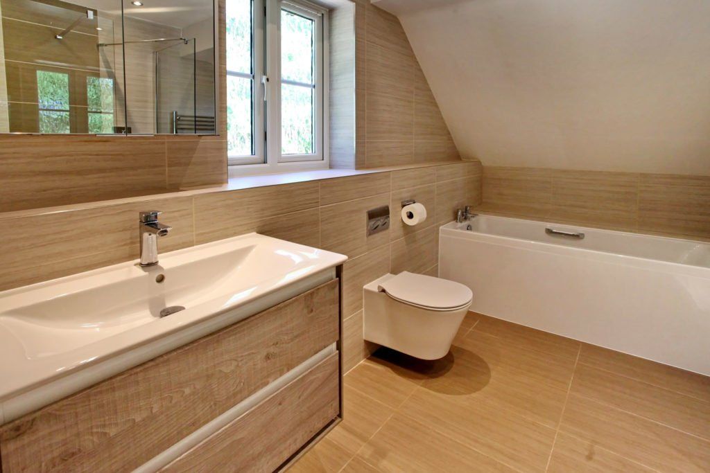 Bathroom with beige tile, white fixtures, wood vanity, and a window.