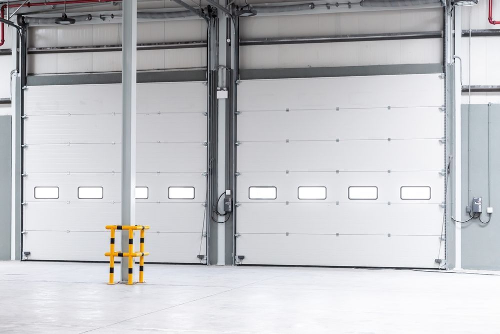 Empty industrial warehouse with two white loading dock doors and yellow safety bollards